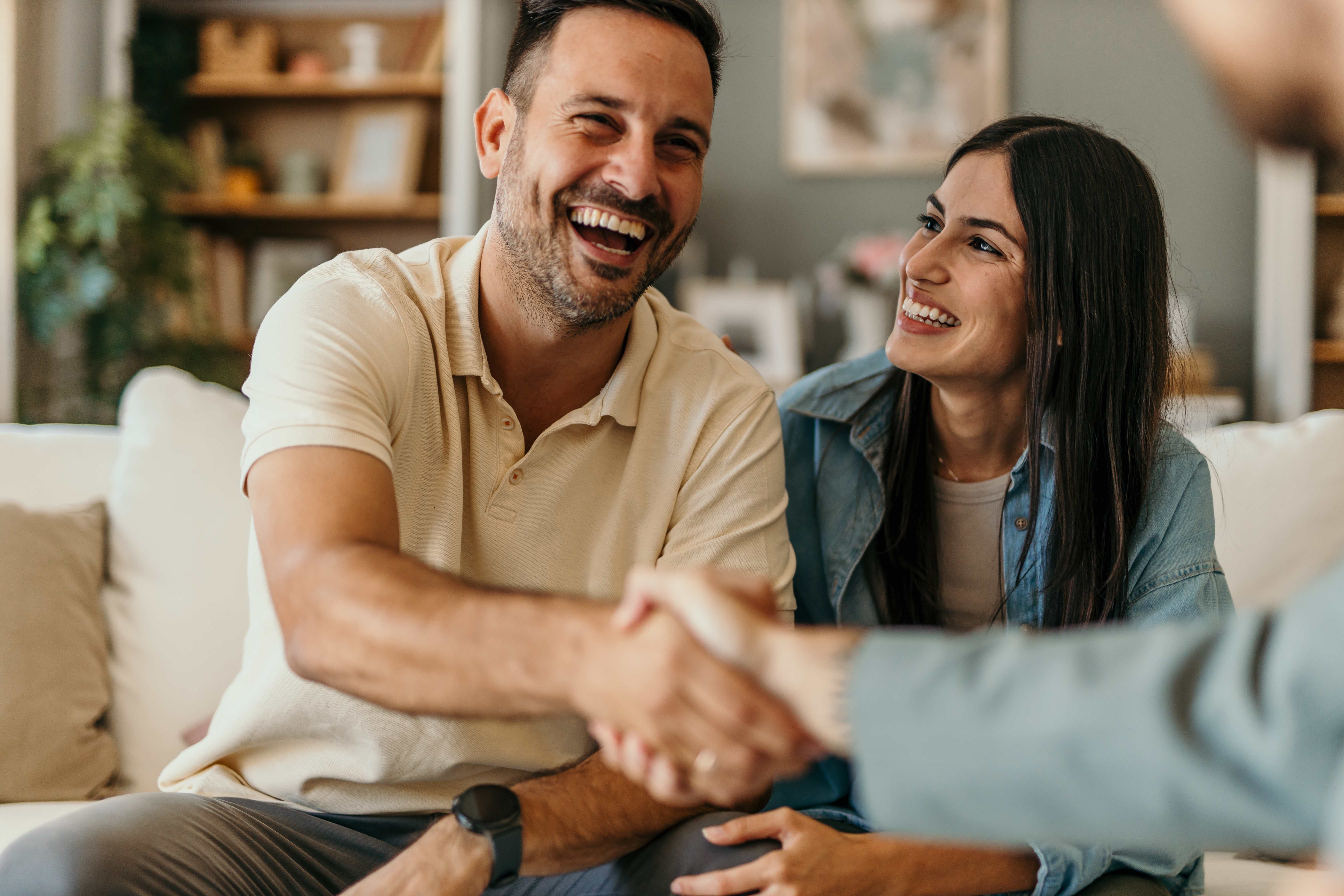 Happy couple shaking hands with property manager in welcoming meeting