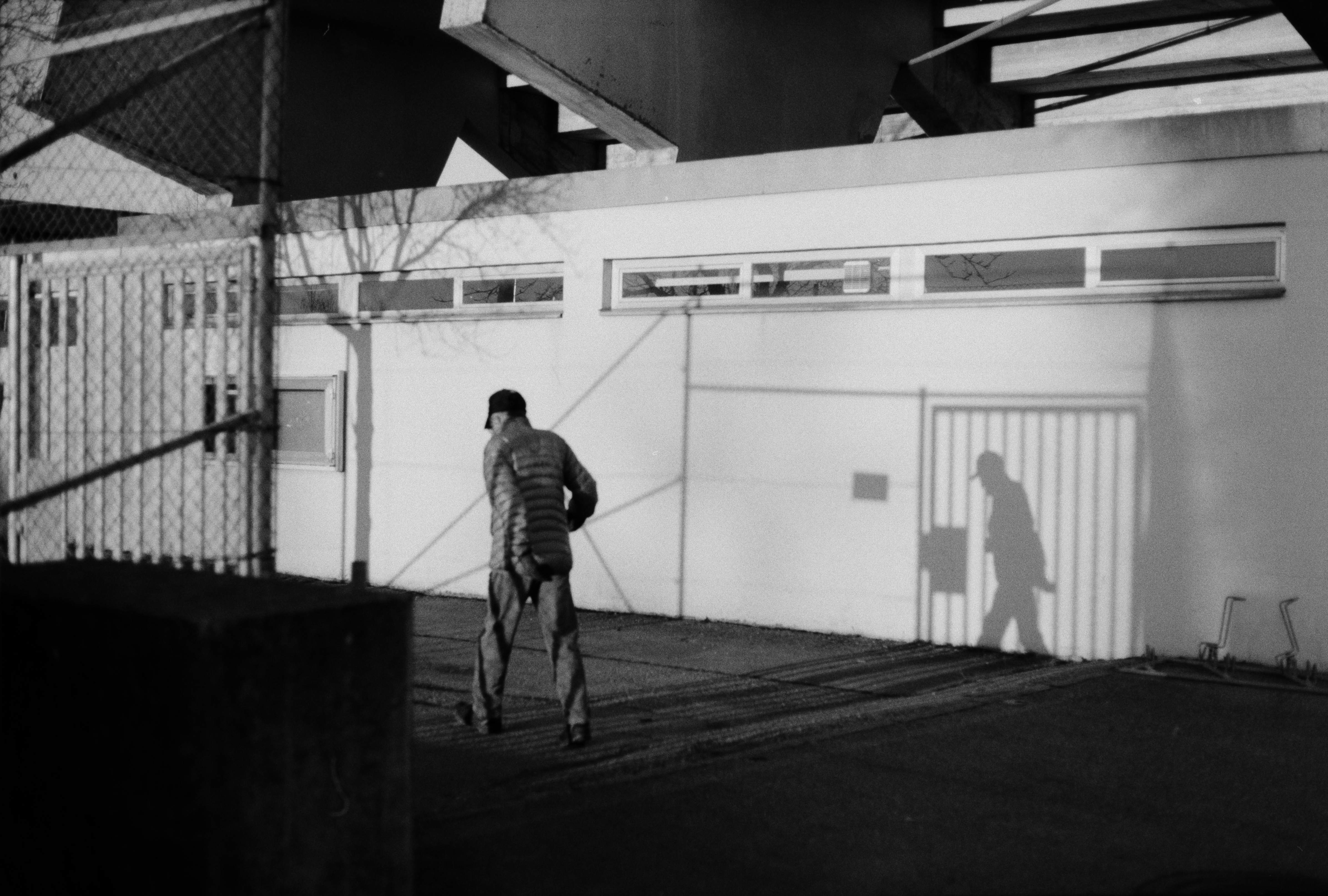Analog black and white street photo of a man walking, casting a long shadow on a white wall