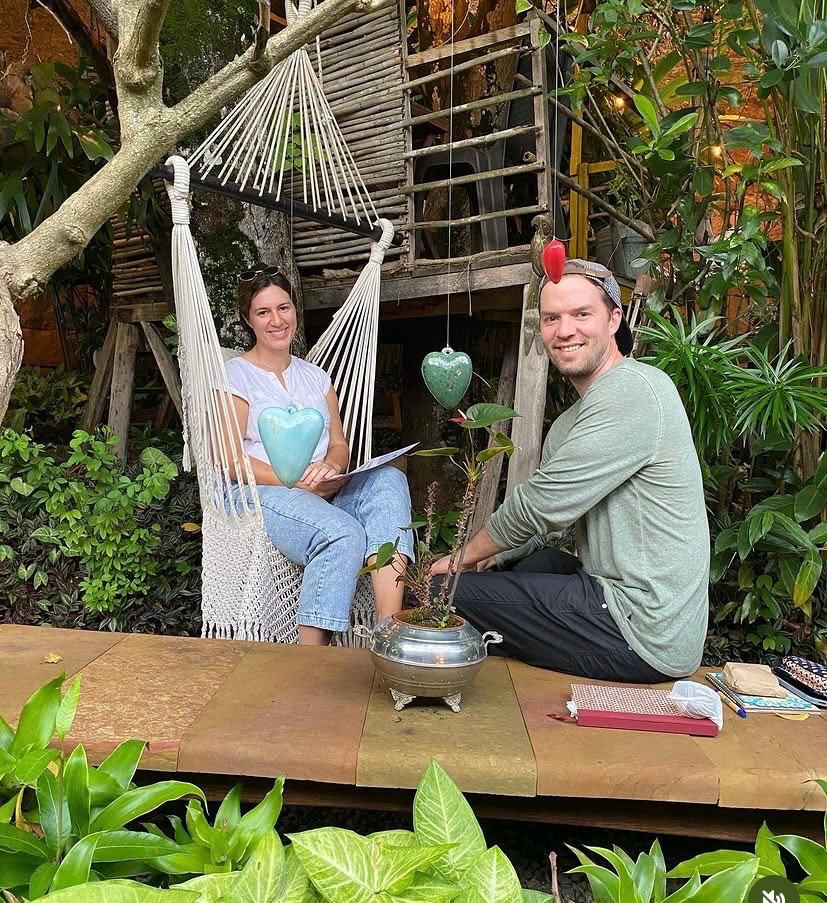 Dos visitantes en La Casita del Árbol: ella en una hamaca de macramé sosteniendo un corazón de cerámica, él sentado en el piso junto a una planta