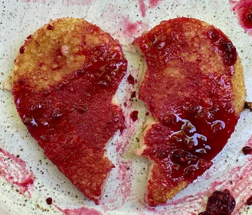 Dos pancakes en forma de corazón bañados en salsa roja de frutos silvestres sobre un plato de cerámica artesanal