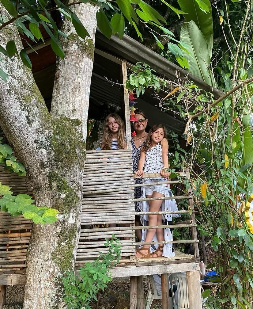 Madre y dos niñas posando desde la terraza de La Casita del Árbol, entre plantas tropicales y bambú