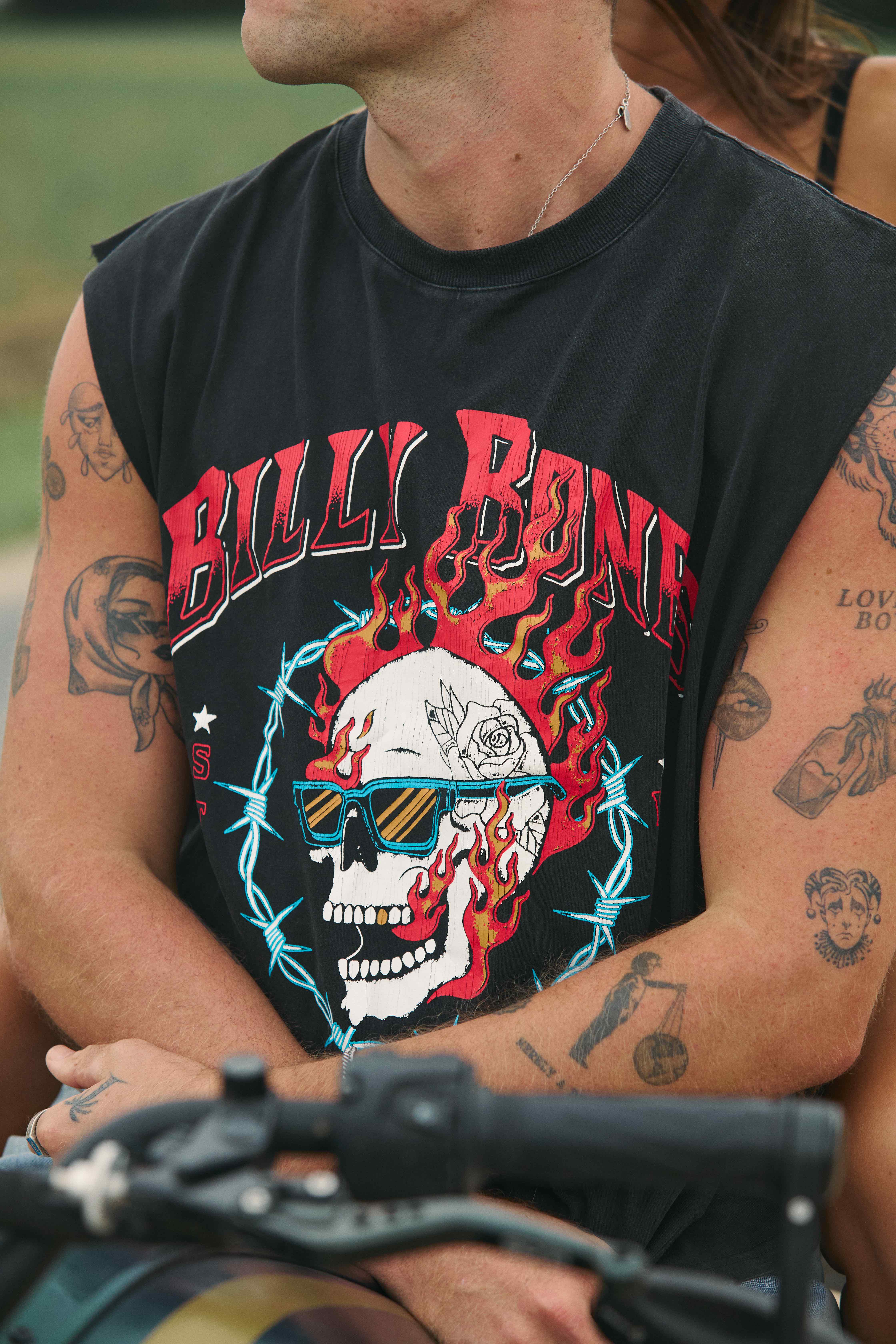 Close-up tattooed male in Billy Bones flaming skull sleeveless tee on motorcycle