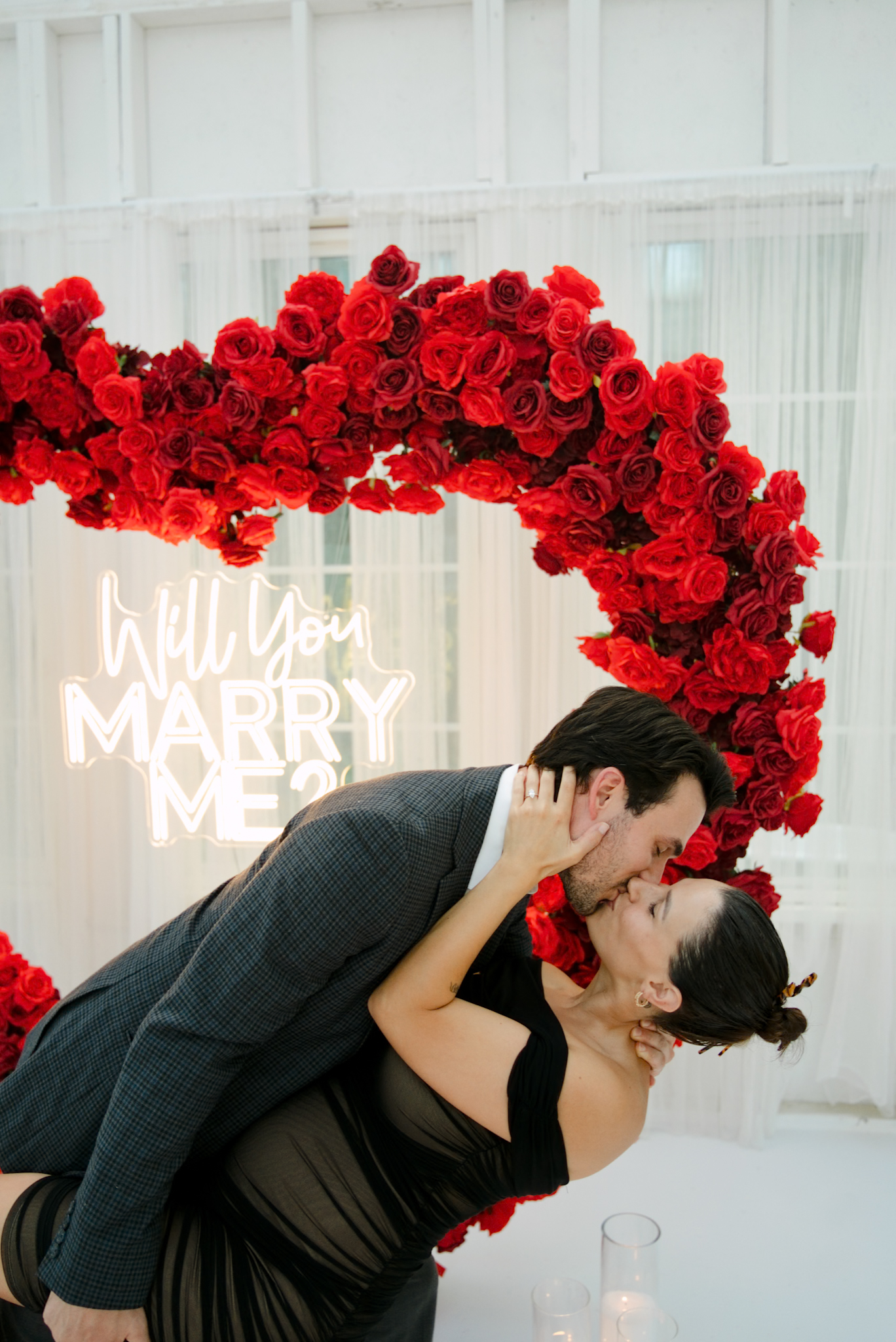 Couple sharing a dramatic dip kiss beneath the rose heart in the glass house