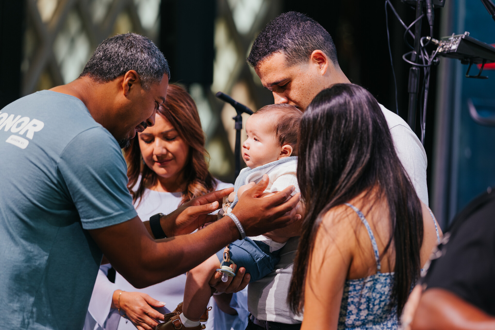 A family dedicating their baby on stage while a pastor prays over them