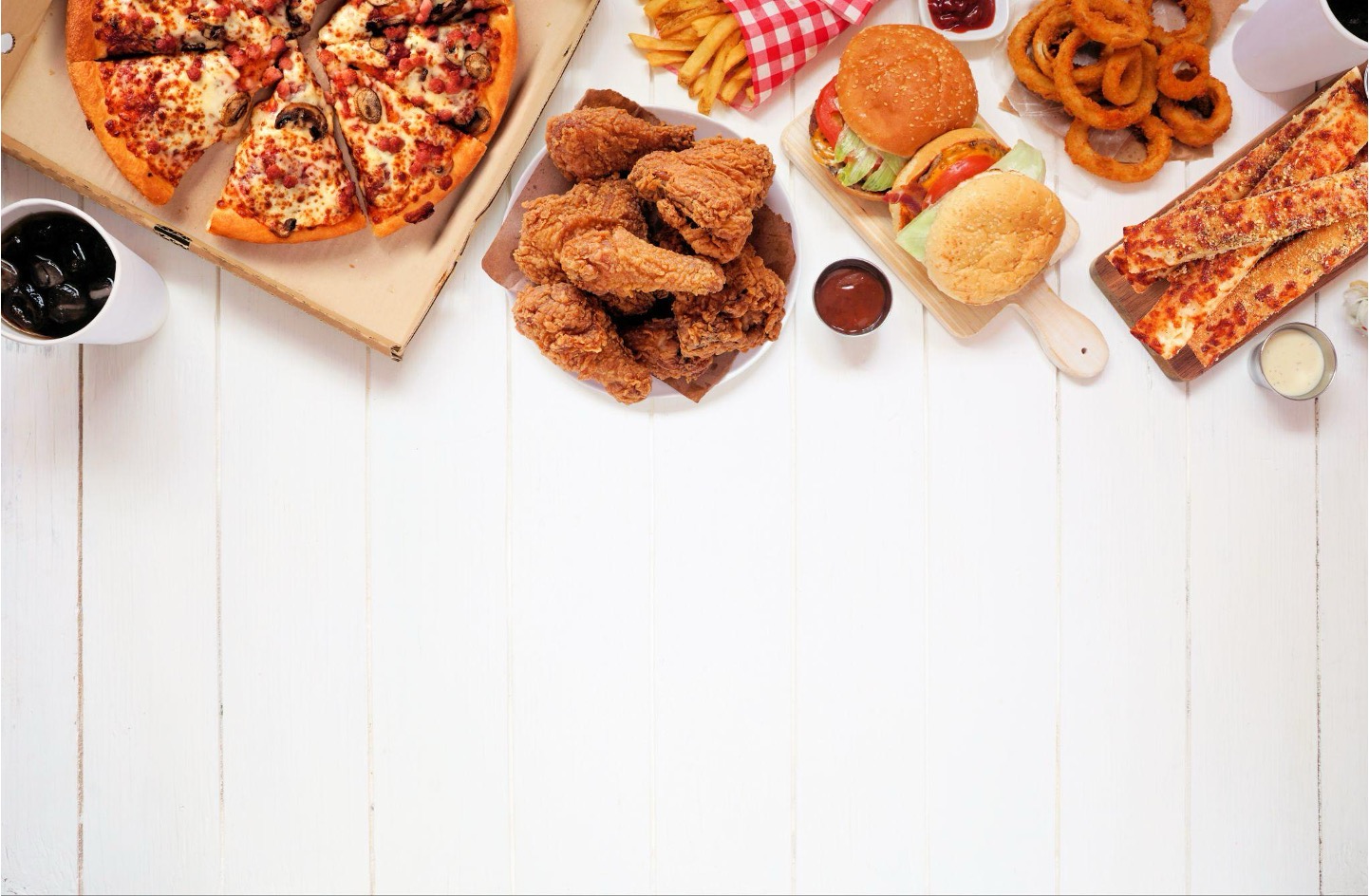 Various fast food items including pizza, fried chicken, burgers, and sides arranged on a white wooden surface