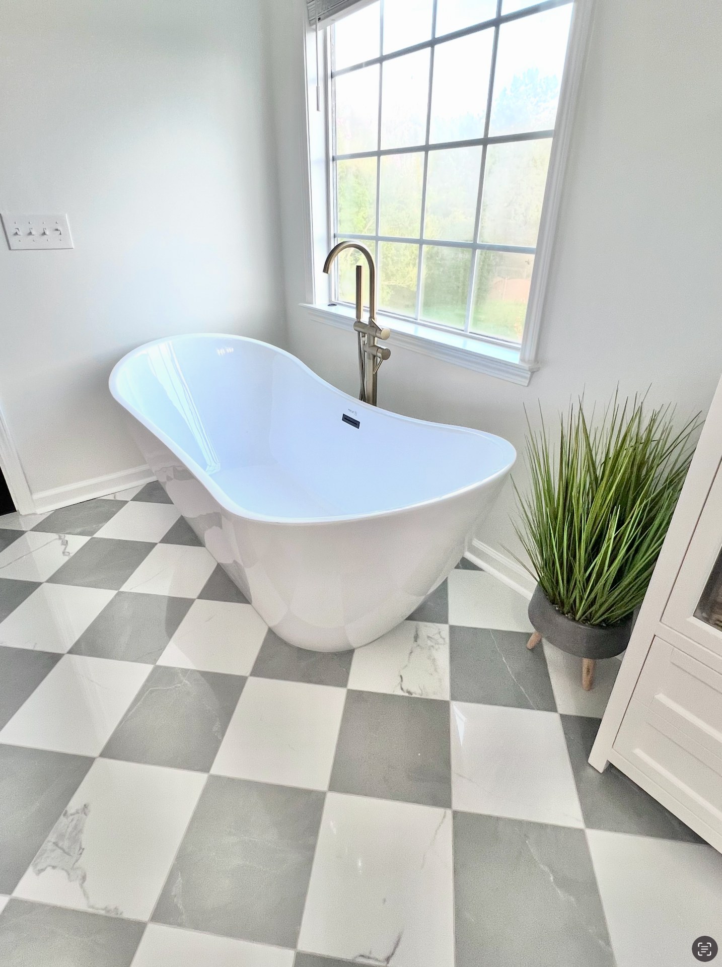 Freestanding slipper tub beneath a divided-light window on a gray-and-white checkerboard marble floor