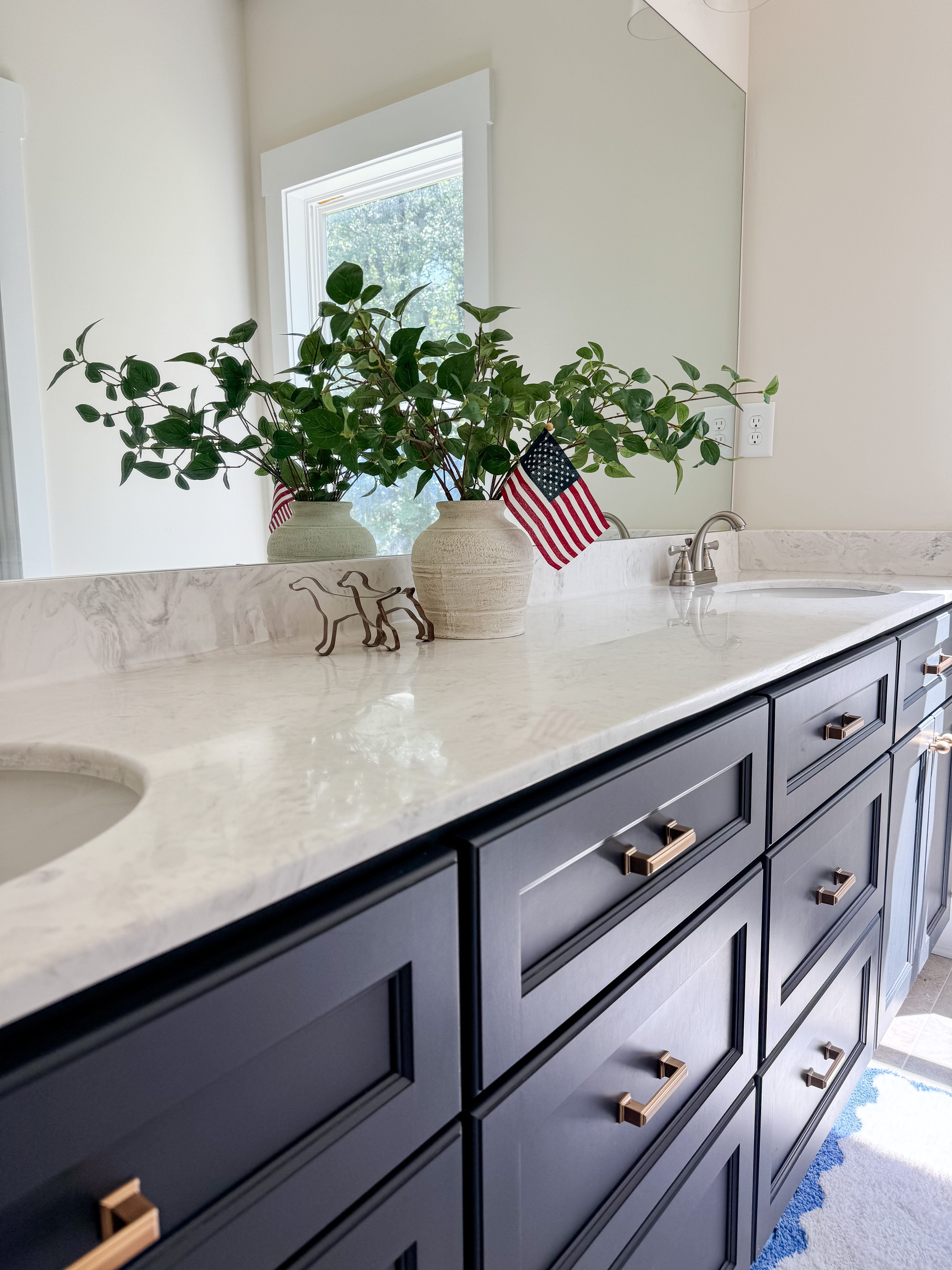 Renovated bathroom with a navy double vanity, marble counter, and frameless mirror