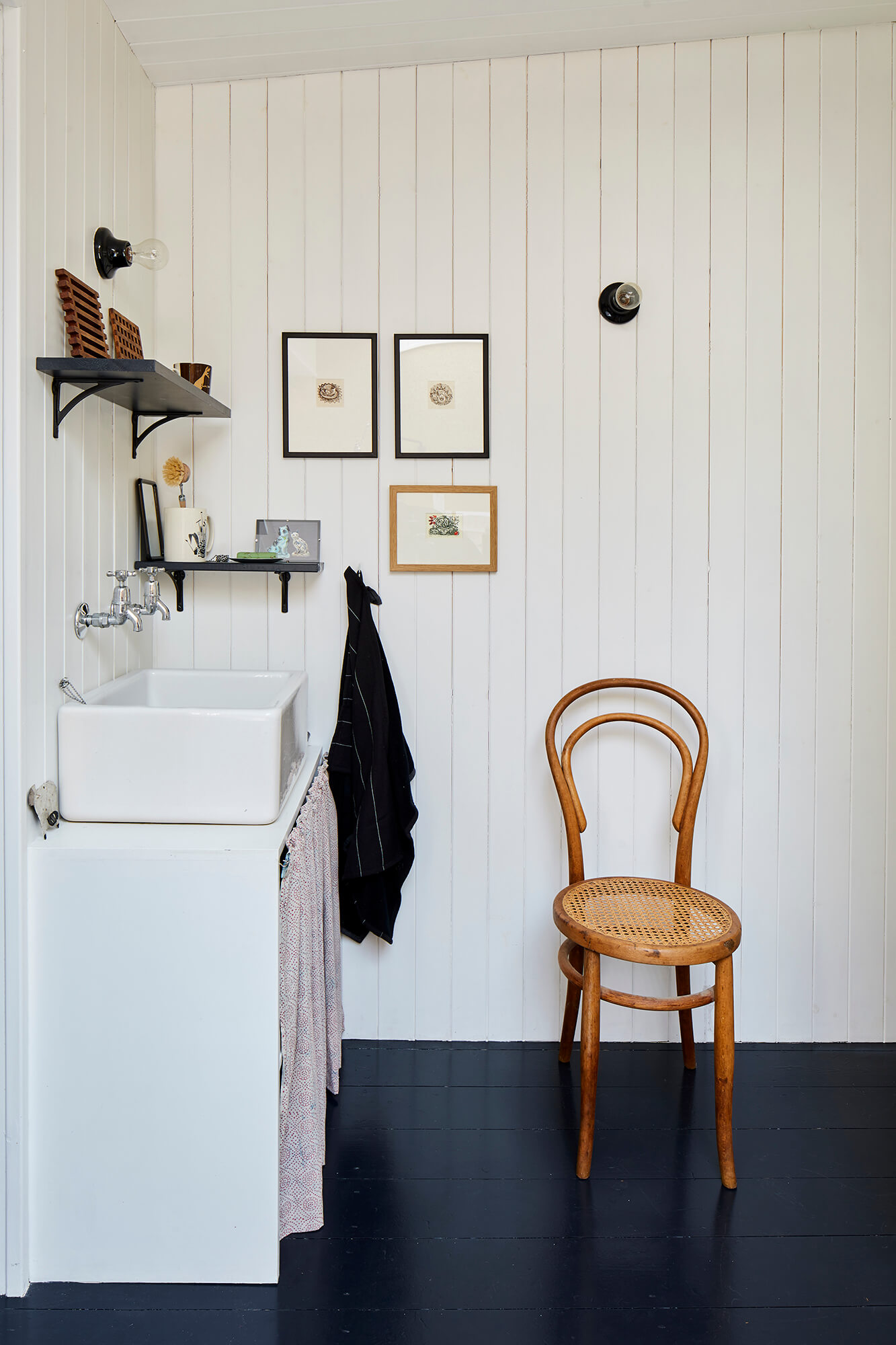 Utility room with white butler sink, black painted floor, and vintage bentwood chair against white paneled walls