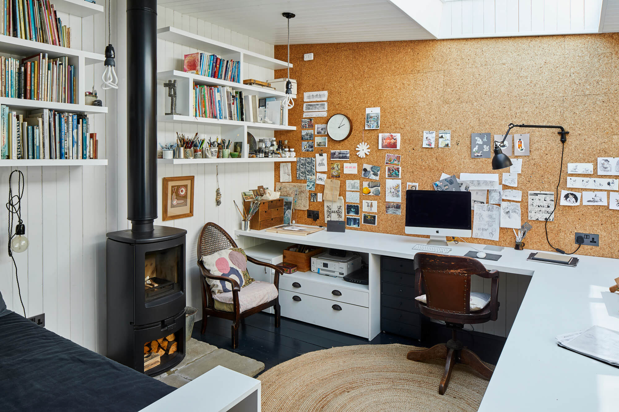 Home office with cork wall display, built-in desk, wood-burning stove, and floating shelves filled with books