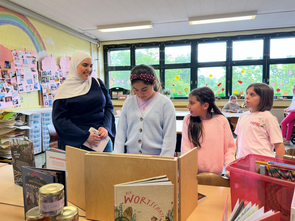Patin und drei Kinder schauen gemeinsam in die aufgeklappte Mini-Bibliothek mit dem Buch "Der Wortschatz"