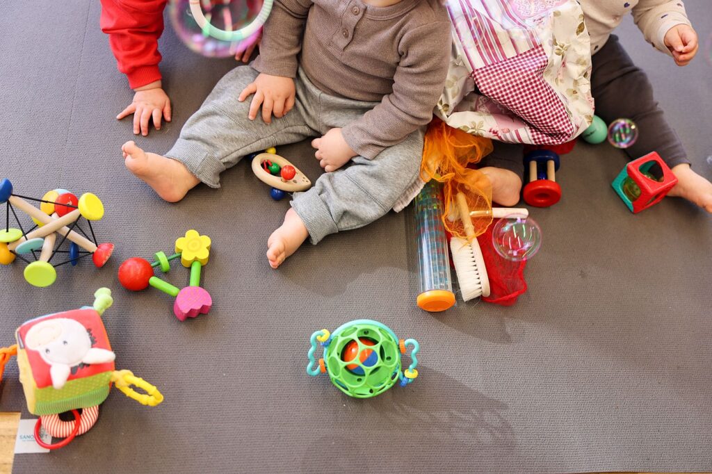 Kleinkinder sitzen auf einer Spielmatte im Krabbelraum des Bonni und erkunden buntes Holzspielzeug