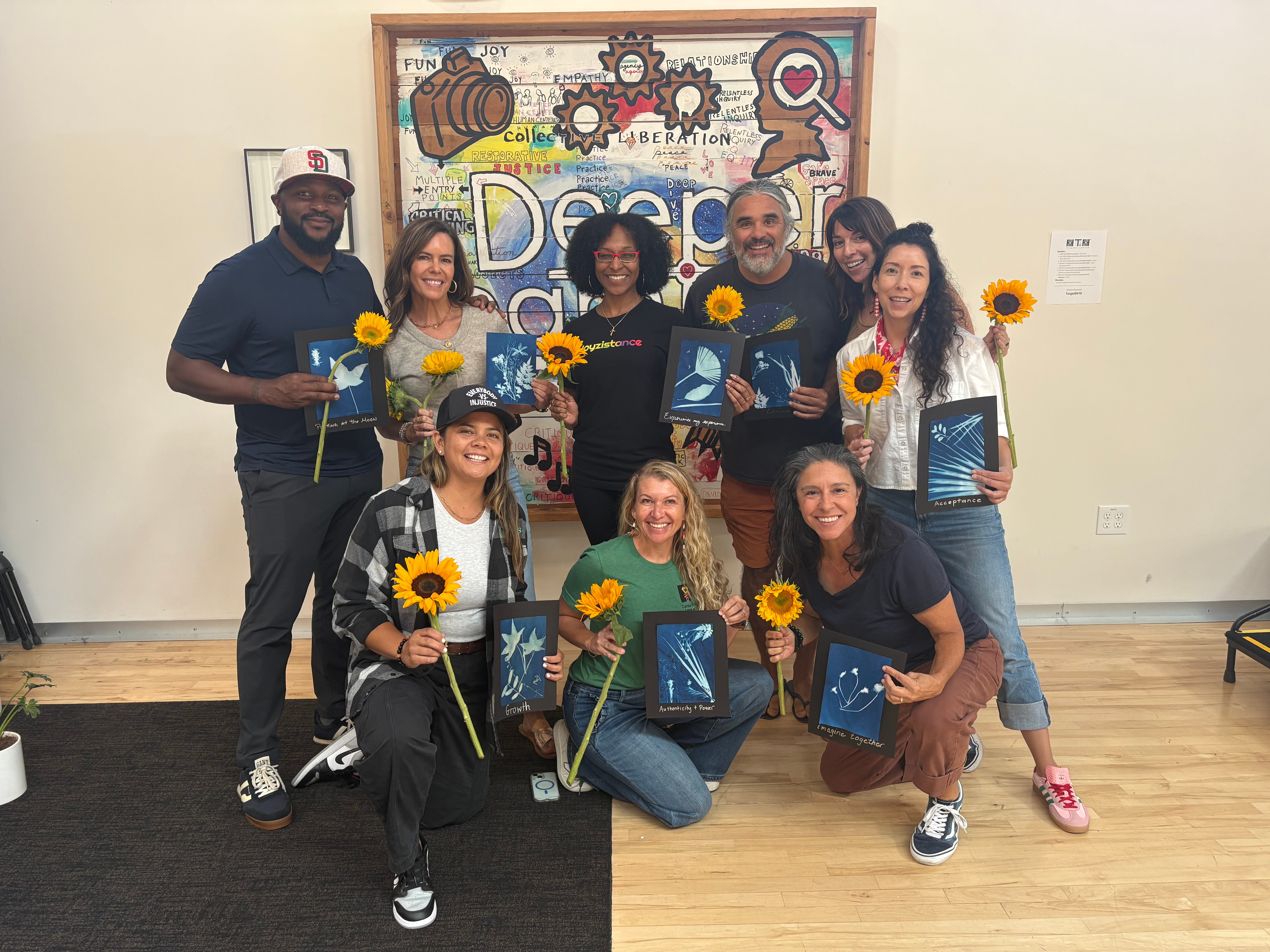 CLJ team members holding sunflowers and cyanotype prints at the September 2025 Advance in front of a colorful Deeper Learning mural