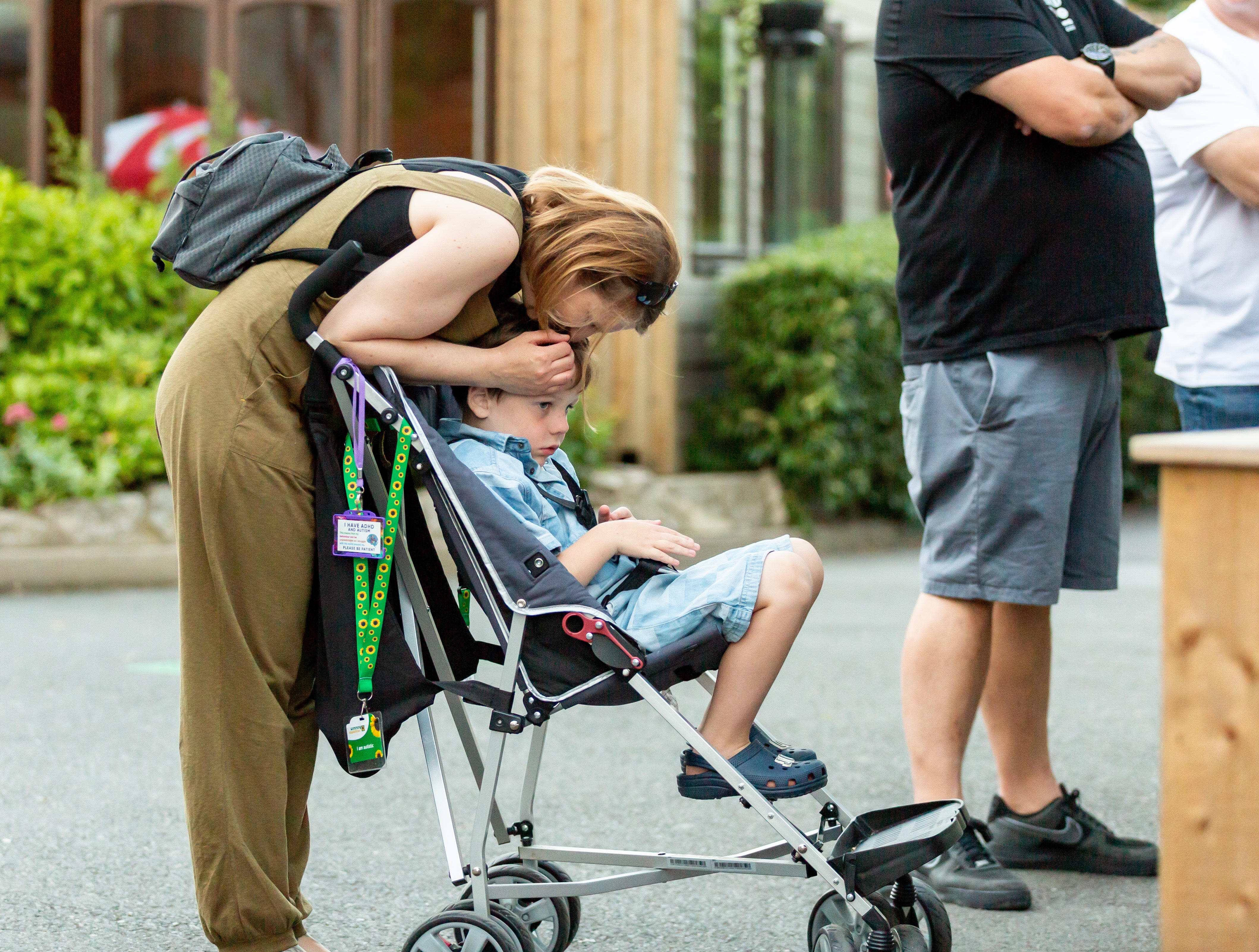 Mother bending down to comfort her young child in a pushchair with sunflower lanyard
