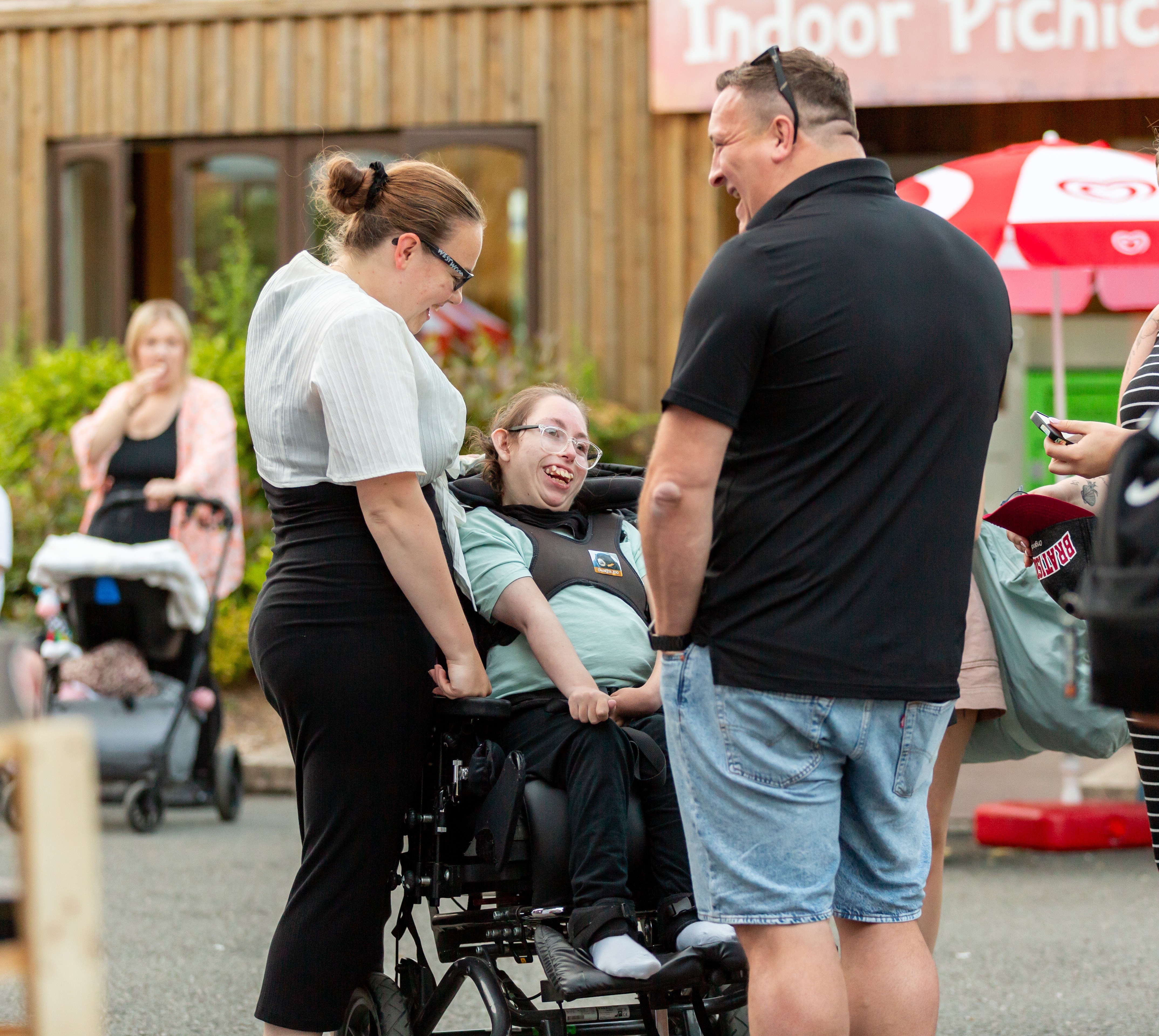 Young woman in a wheelchair laughing with a carer and family member outdoors