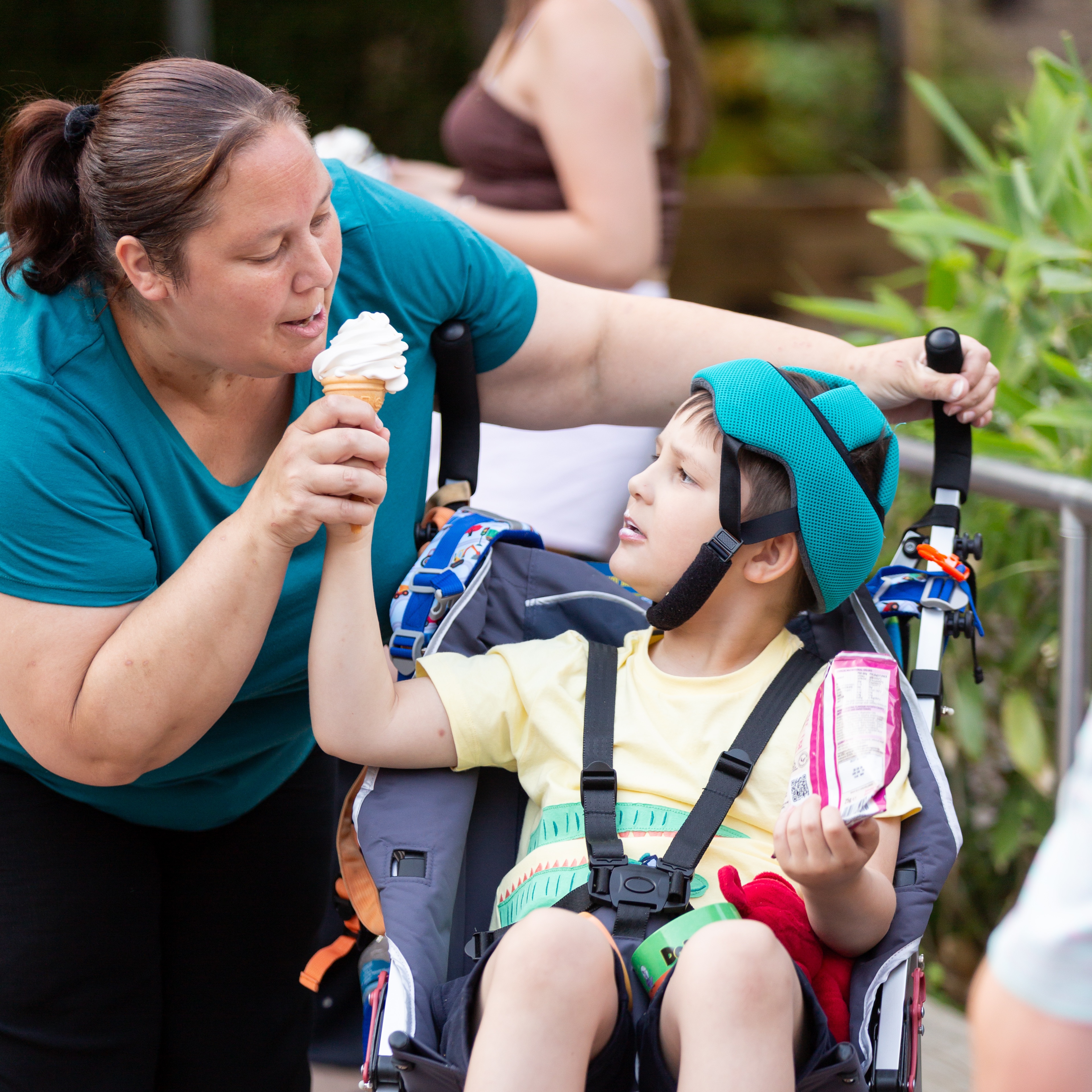 Carer sharing an ice cream with a child in an adapted wheelchair at a SEND Fest event