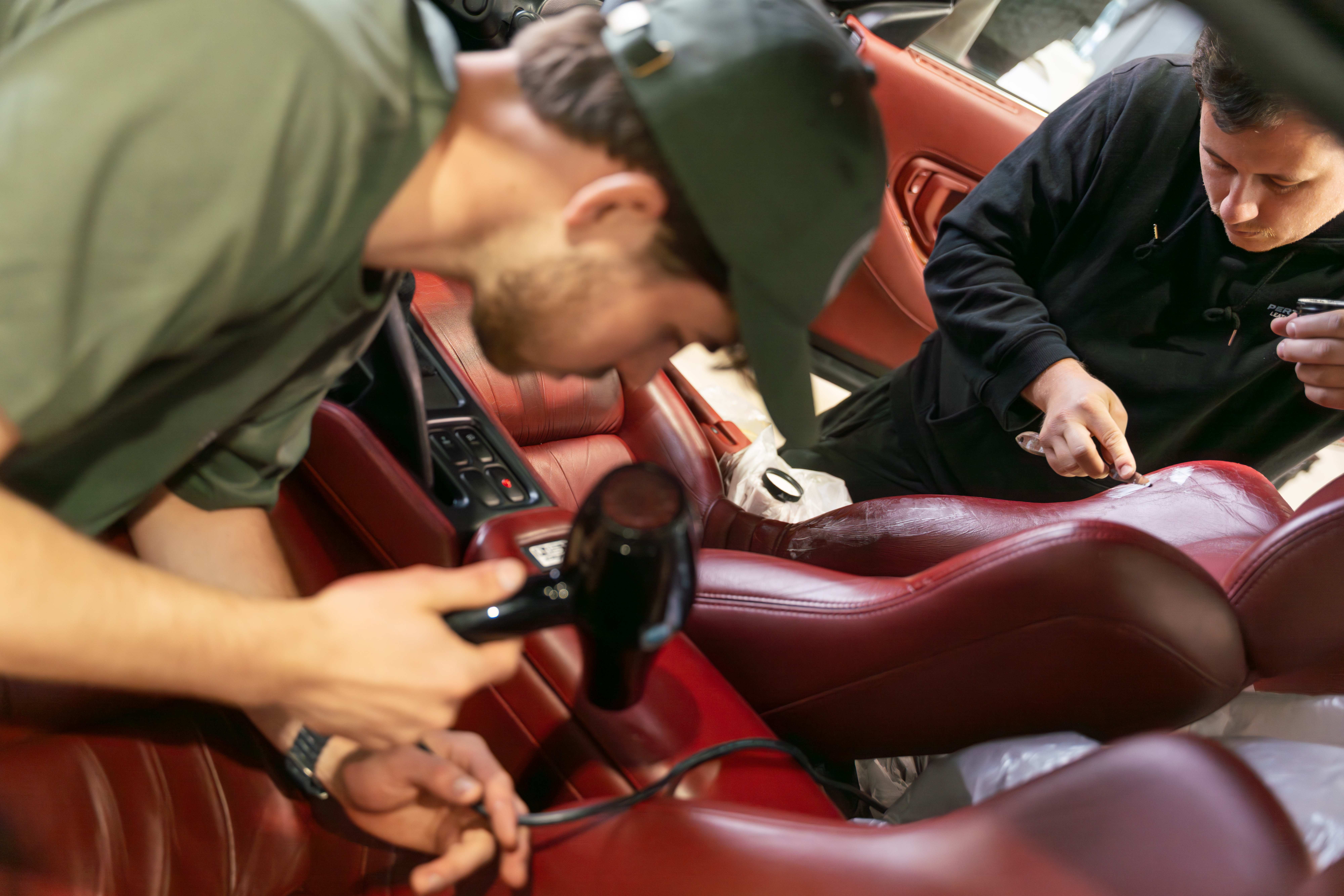 Two leather repair technicians working on burgundy sports car interior seat restoration