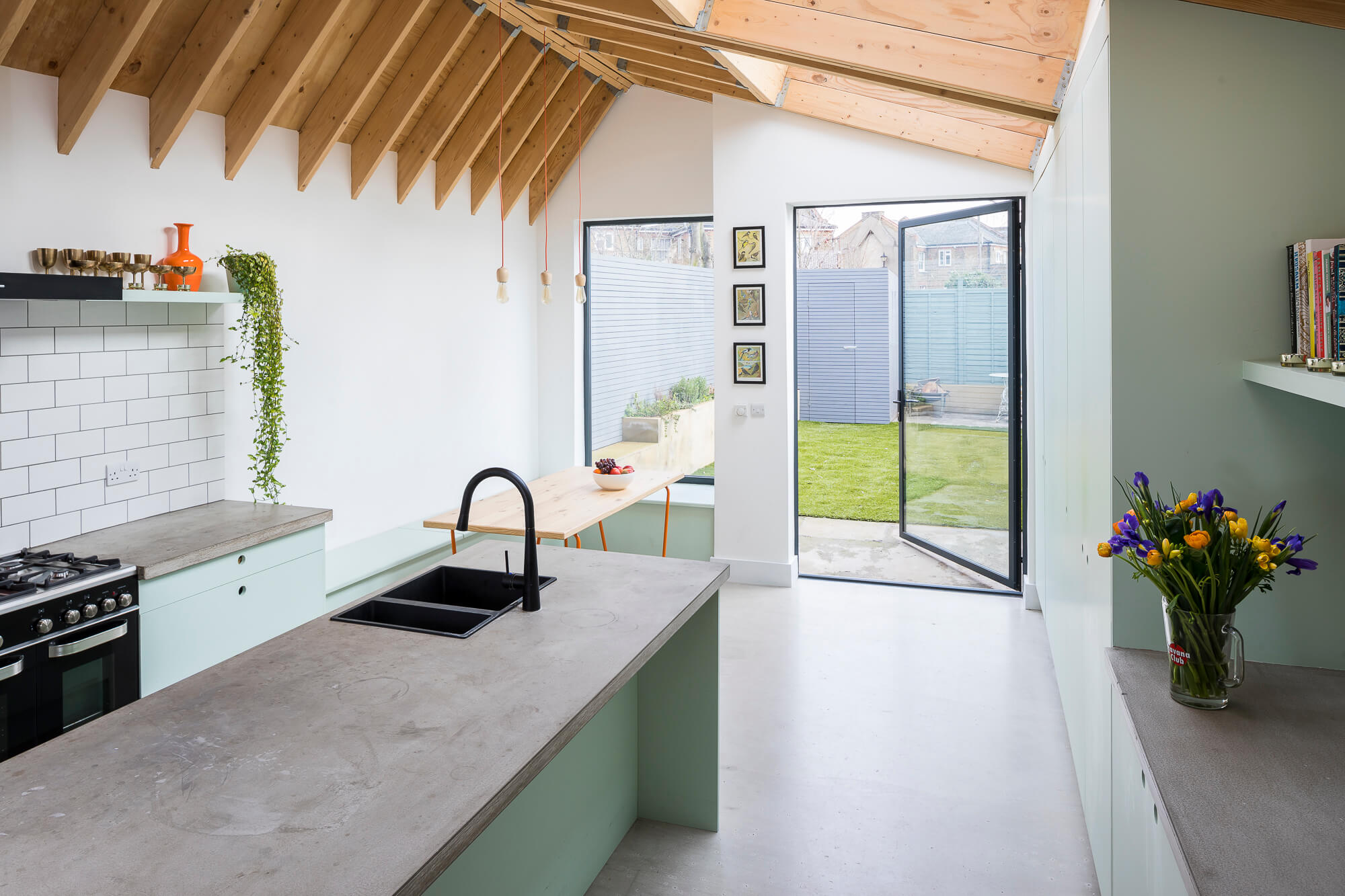 Modern kitchen extension with mint green cabinets, concrete countertops, and exposed timber ceiling beams