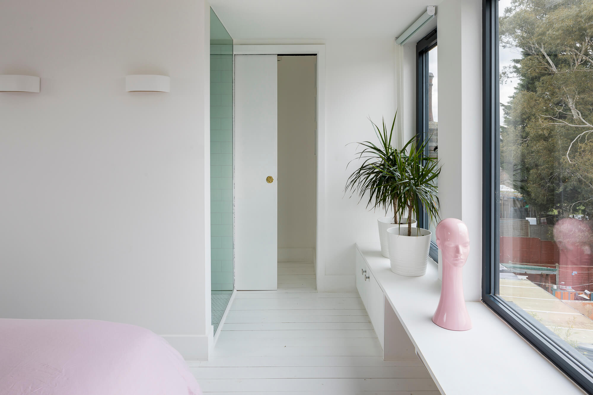 Bedroom with sliding door to mint green tiled bathroom and built-in window seat