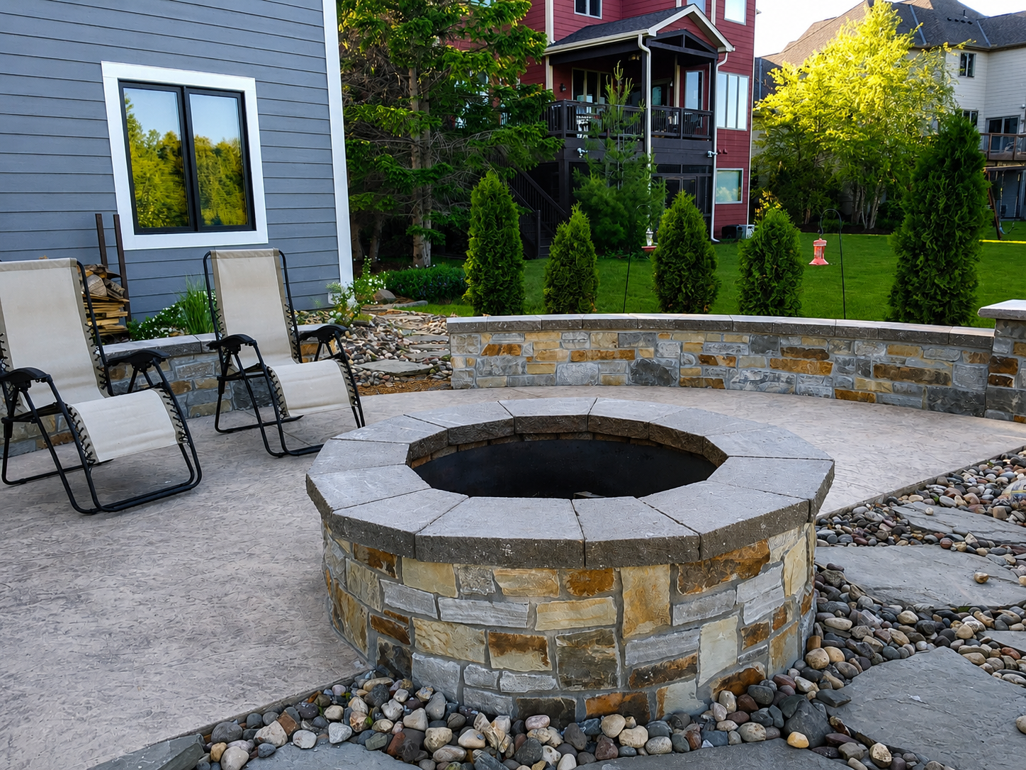 Natural stone outdoor fire circle set into a stamped concrete patio with decorative river stone landscaping.