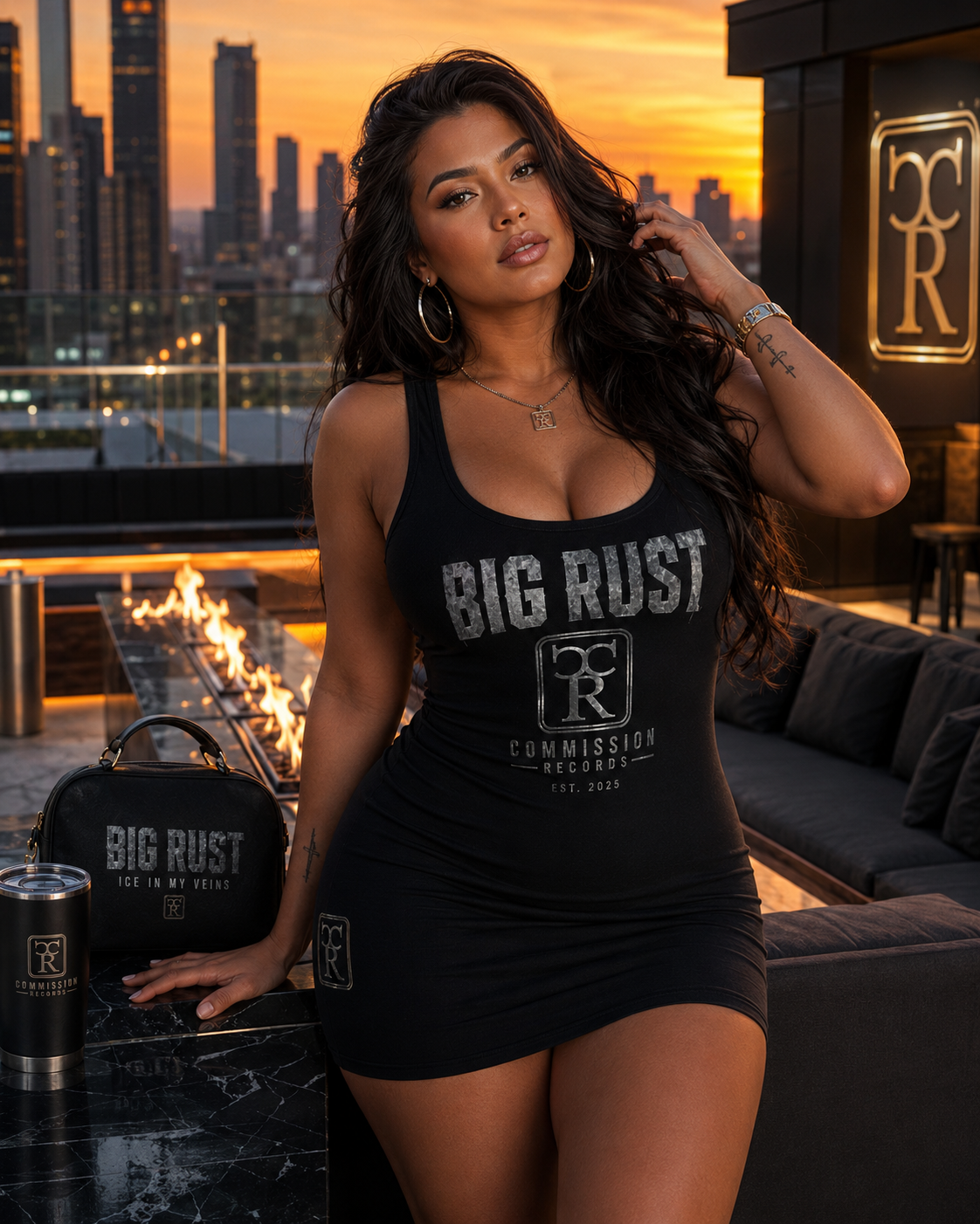 Woman on a rooftop lounge at sunset wearing a black Big Rust Commission Records Est 2025 distressed-print bodycon tank mini dress, beside a black Big Rust Ice In My Veins handbag and a CR tumbler by a fire pit