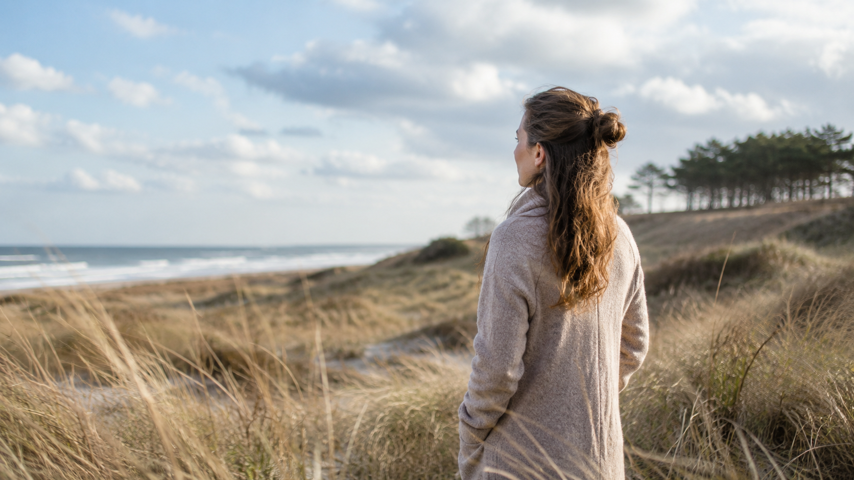 Frau steht in Stranddünen und blickt aufs Meer – Symbol für innere Freiheit und neue Perspektiven durch Hypnosetherapie