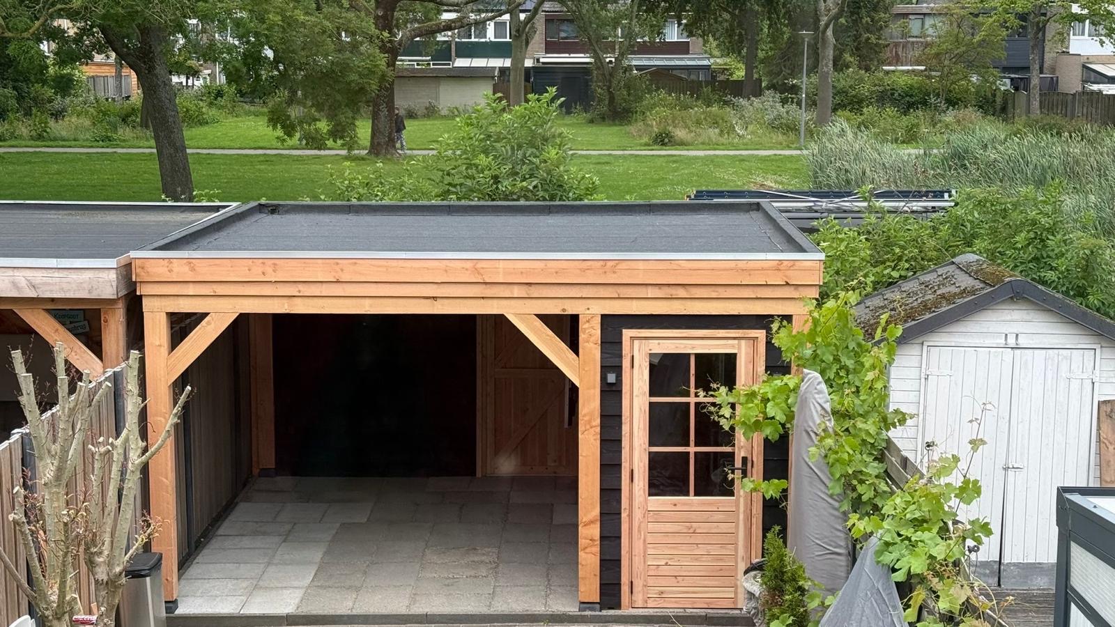 Houten buitenverblijf met garageopening, deur en betegelde vloer in een tuin