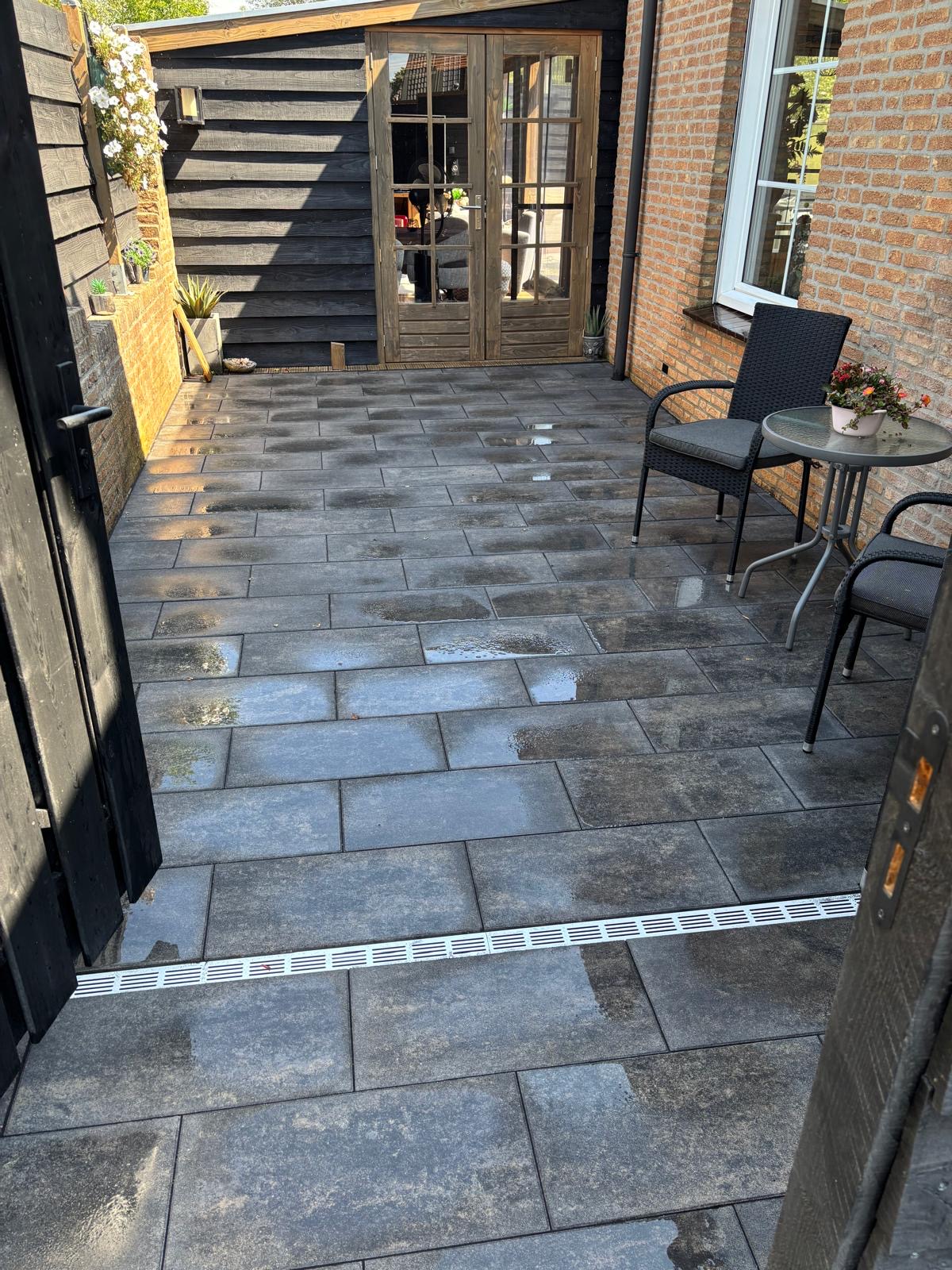 Betegeld terras naast een woning met een donker houten buitenverblijf en glazen deuren