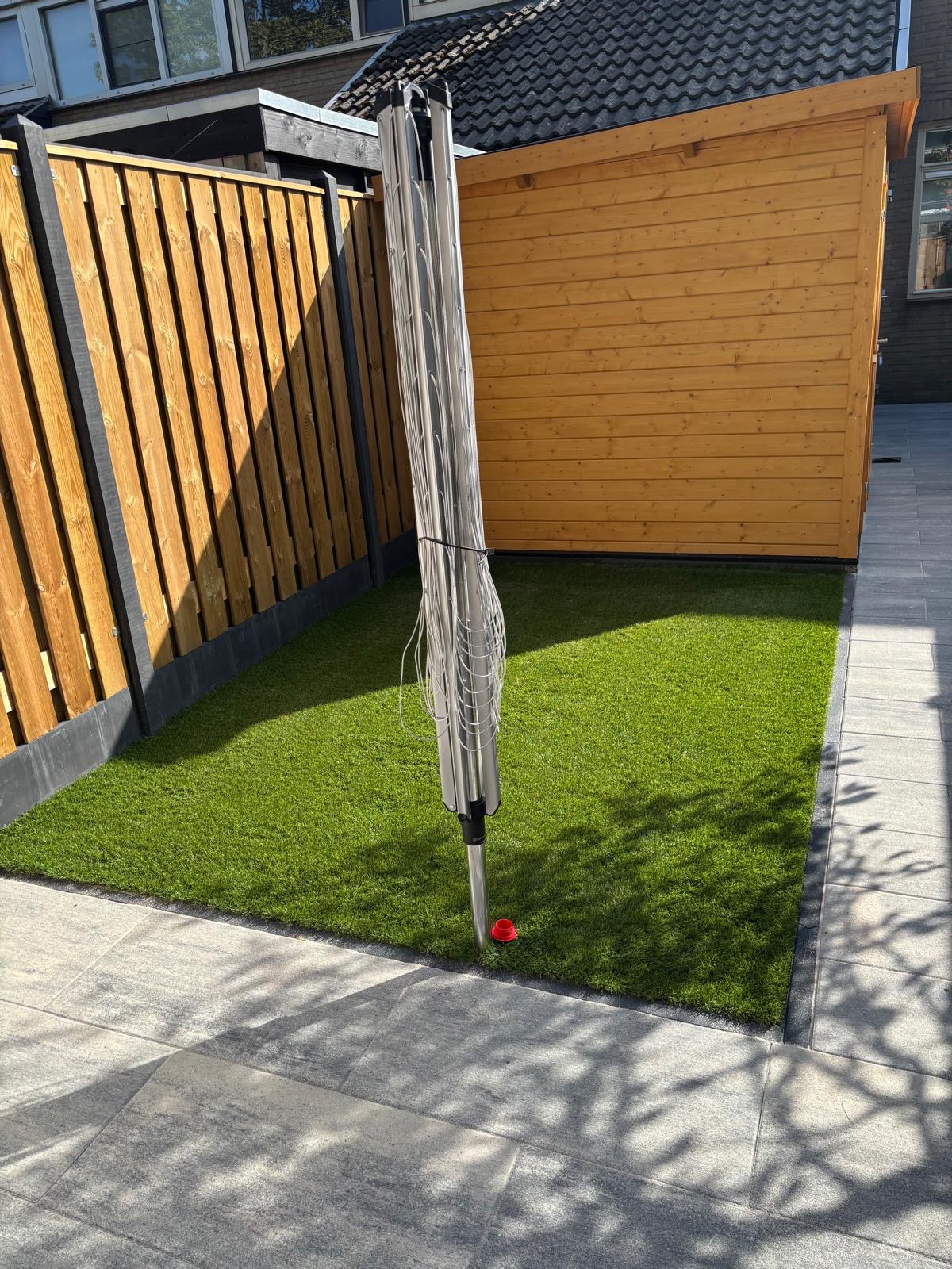 Kunstgrasveld met bestrating en houten schutting in een achtertuin