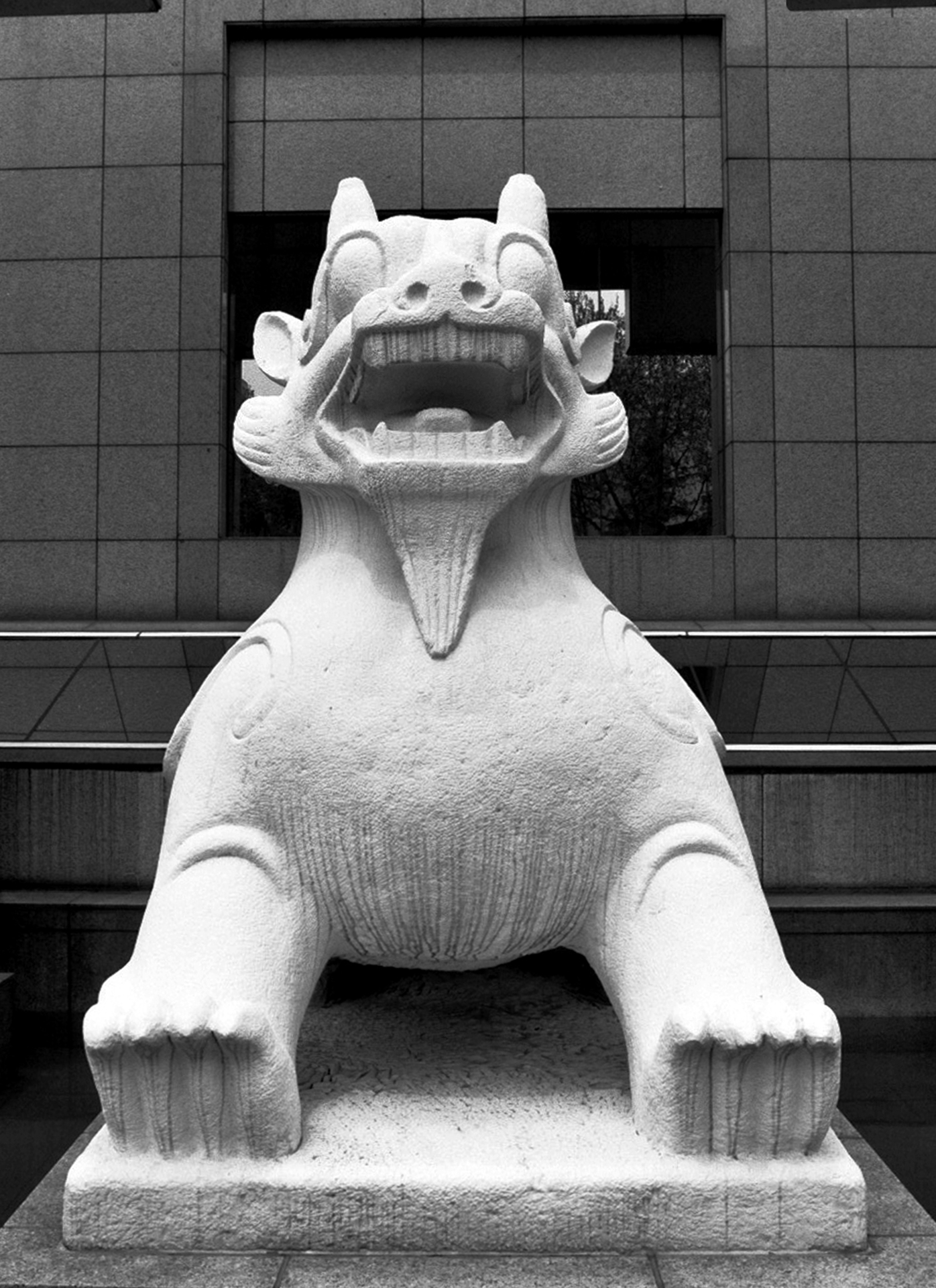 Stone lion guardian statue with open mouth positioned in front of modern building