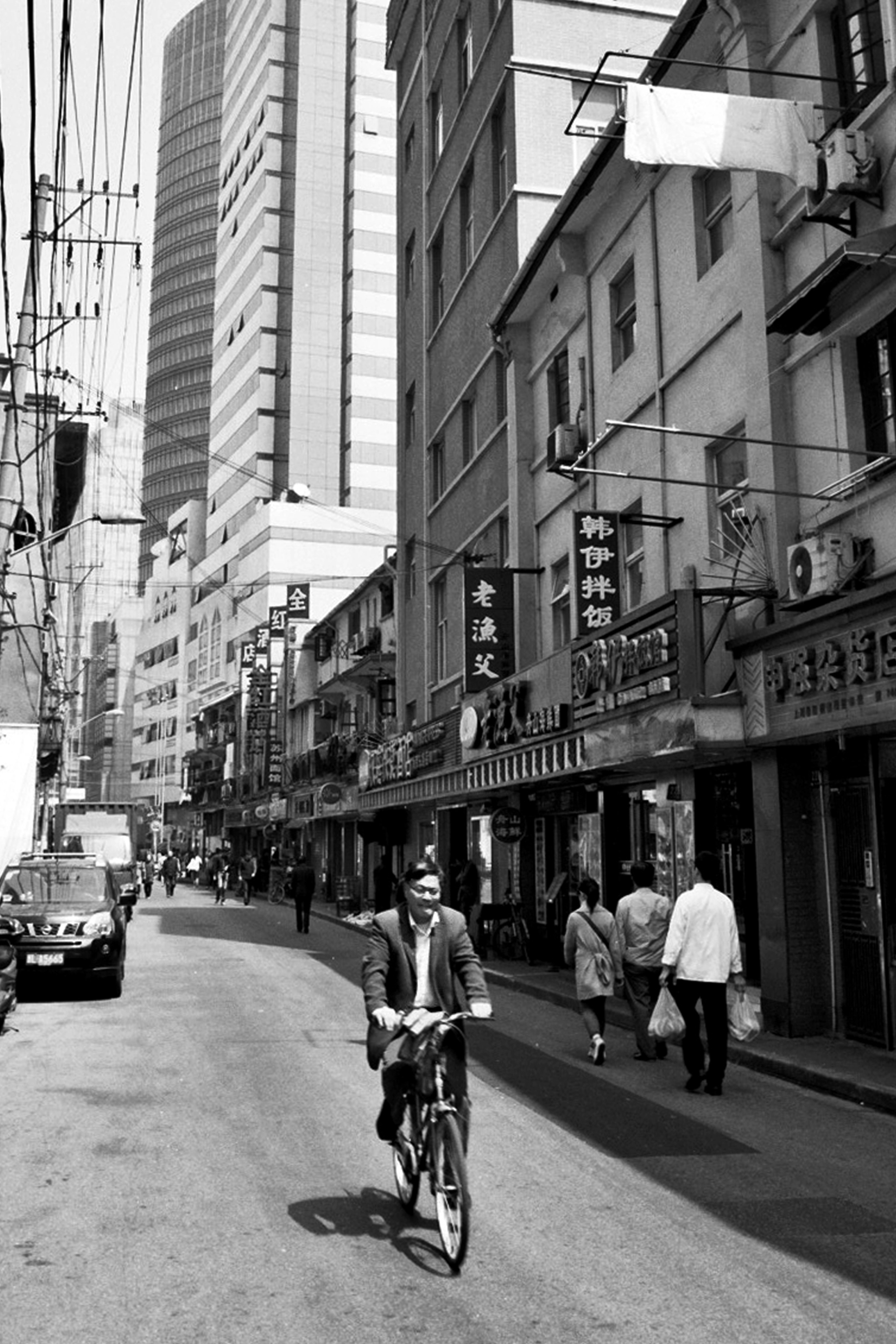 Man riding bicycle down narrow Shanghai street lined with shops and Chinese signage