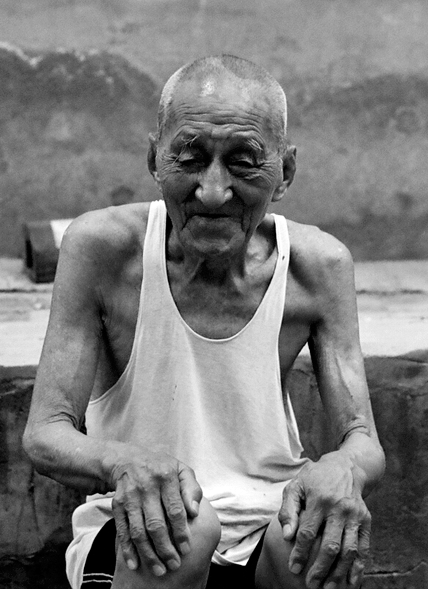 Portrait of elderly man in sleeveless white shirt against mountain background