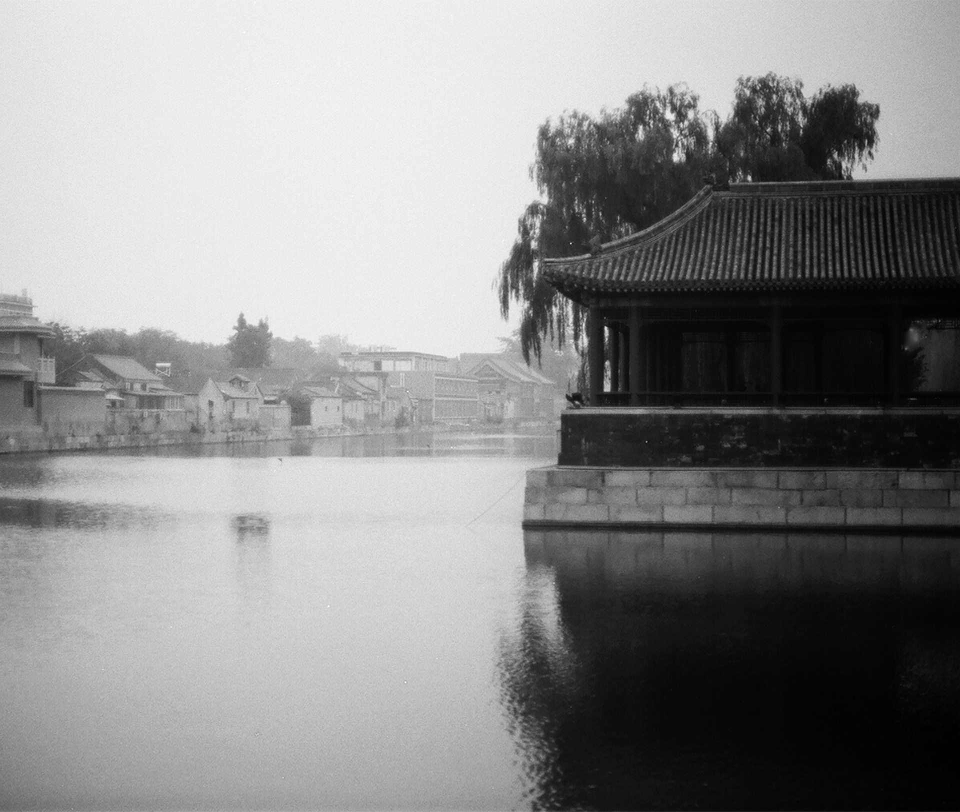 Misty lakeside scene with traditional Chinese pavilion with curved roof and weeping willows