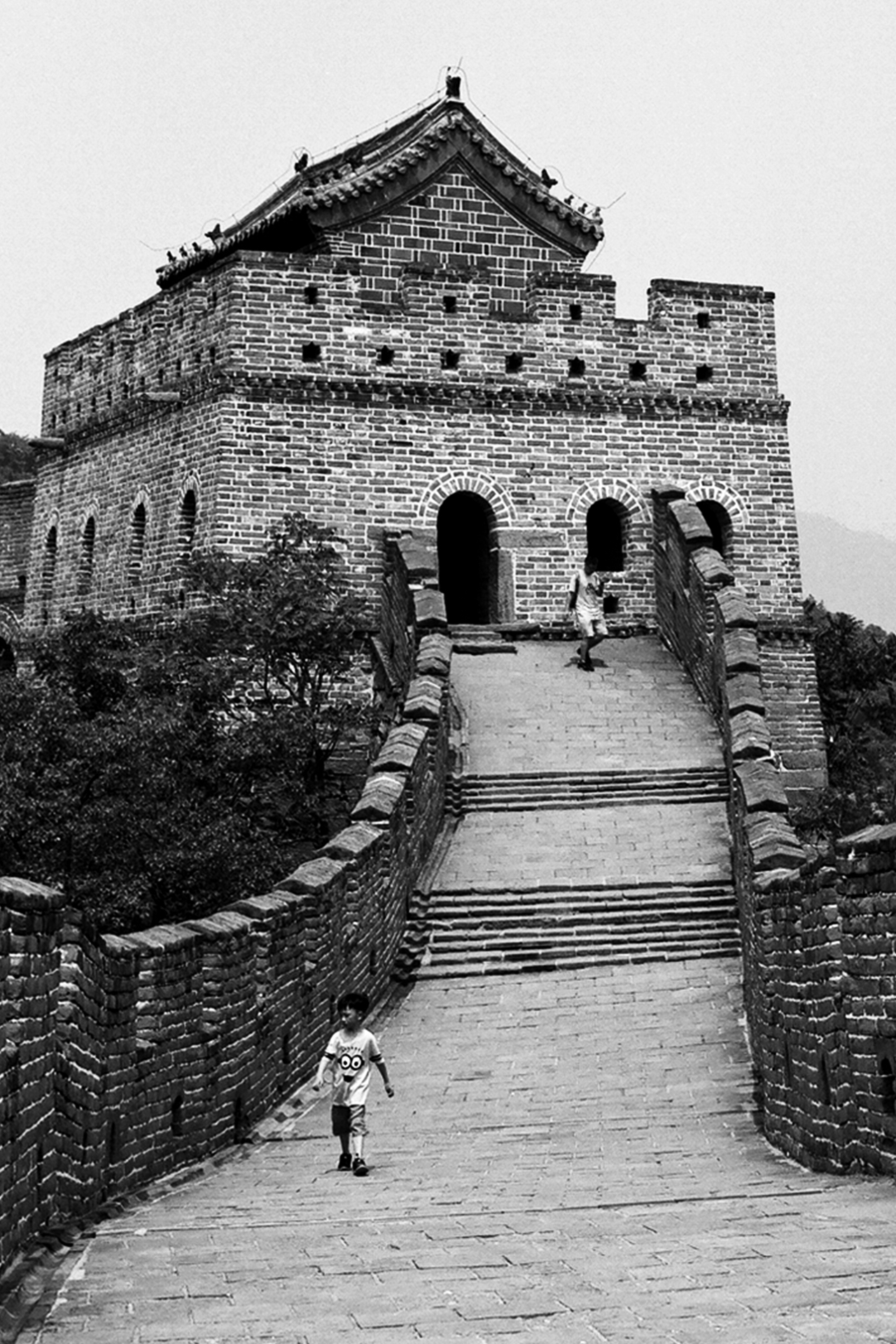 Great Wall of China watchtower with curved roof rising through forested mountains and walkway
