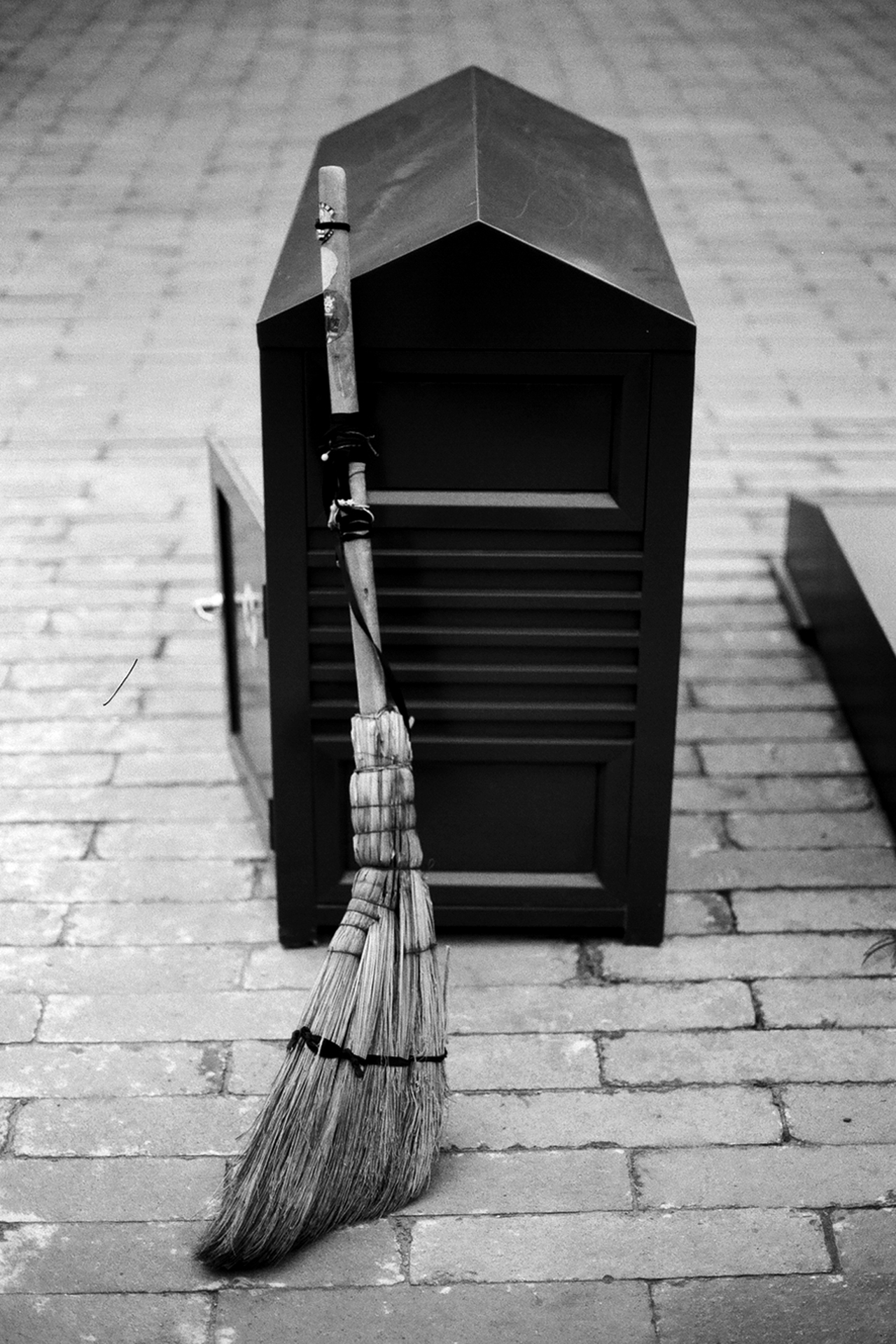 Natural broom leaning against dark wooden storage chest on traditional paved stone surface