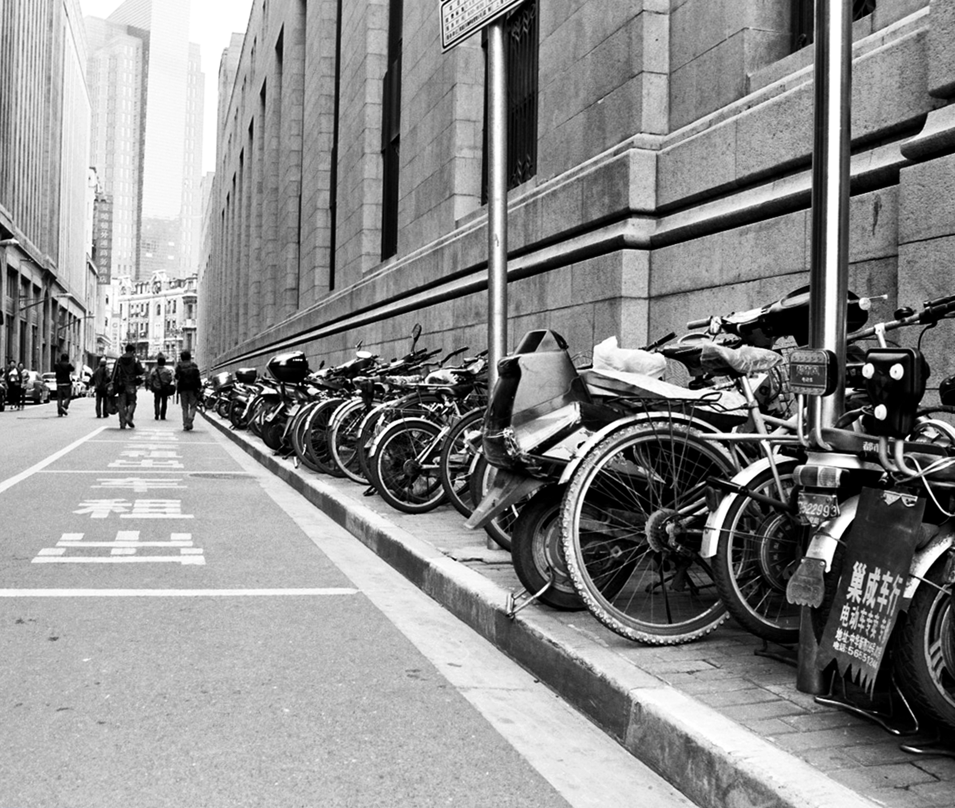 Urban street lined with parked bicycles and motorcycles against modern building facade