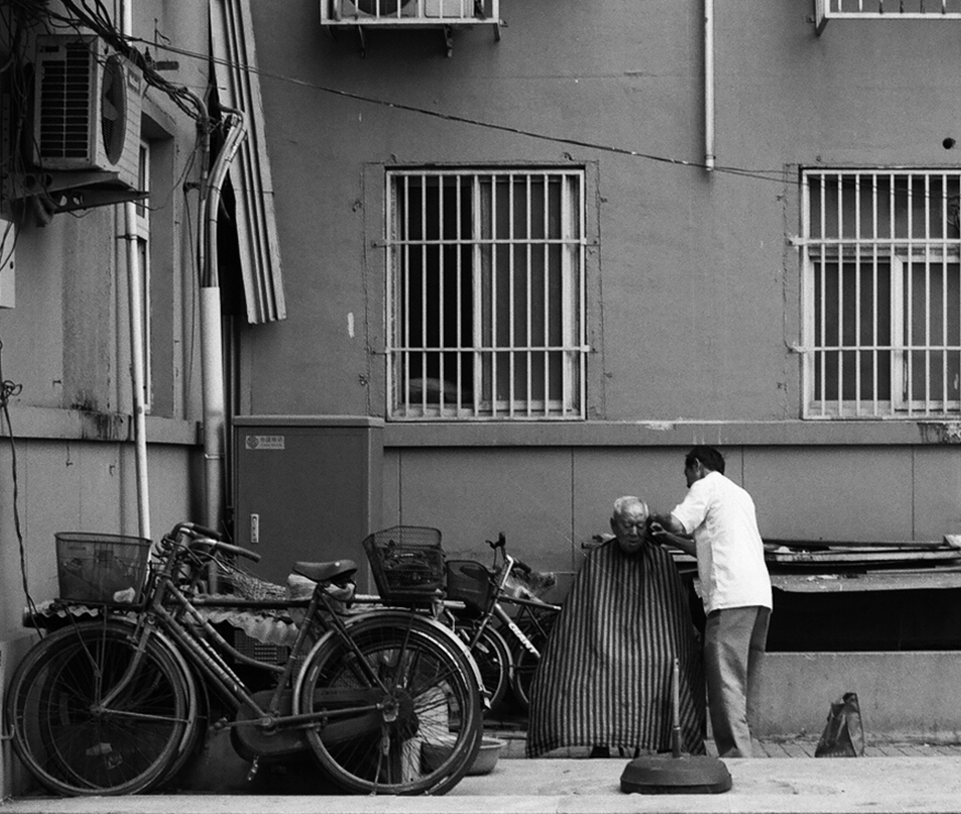 Street scene with elderly man getting haircut by woman among parked bicycles and motorcycles