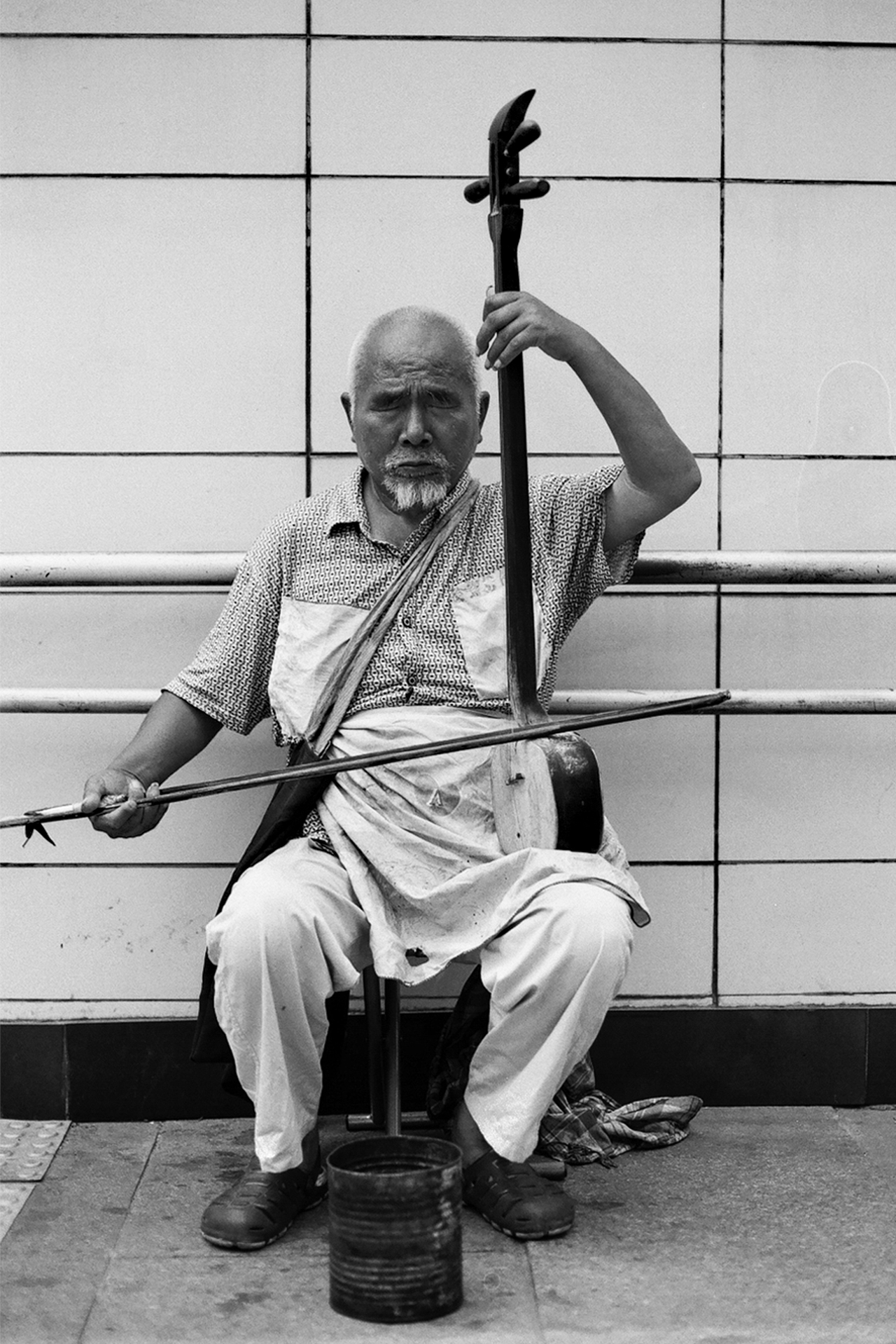 Elderly man sitting with traditional erhu two-string violin instrument against gridded wall