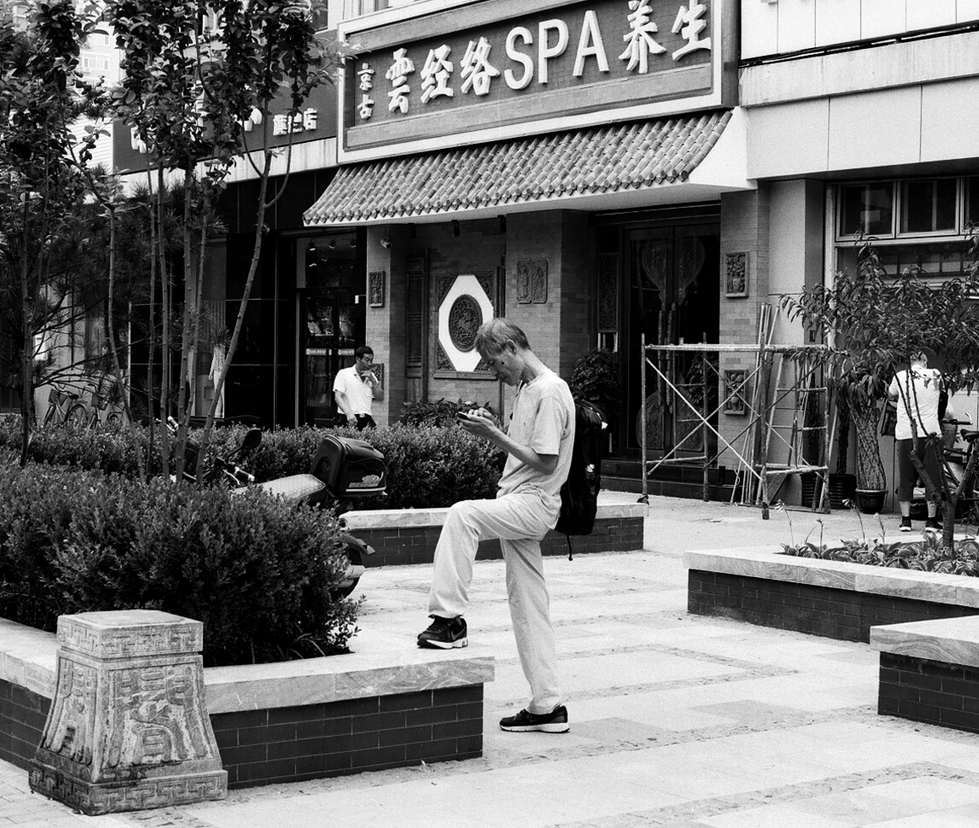 Man in white shirt performing tai chi martial arts movement in plaza with traditional building
