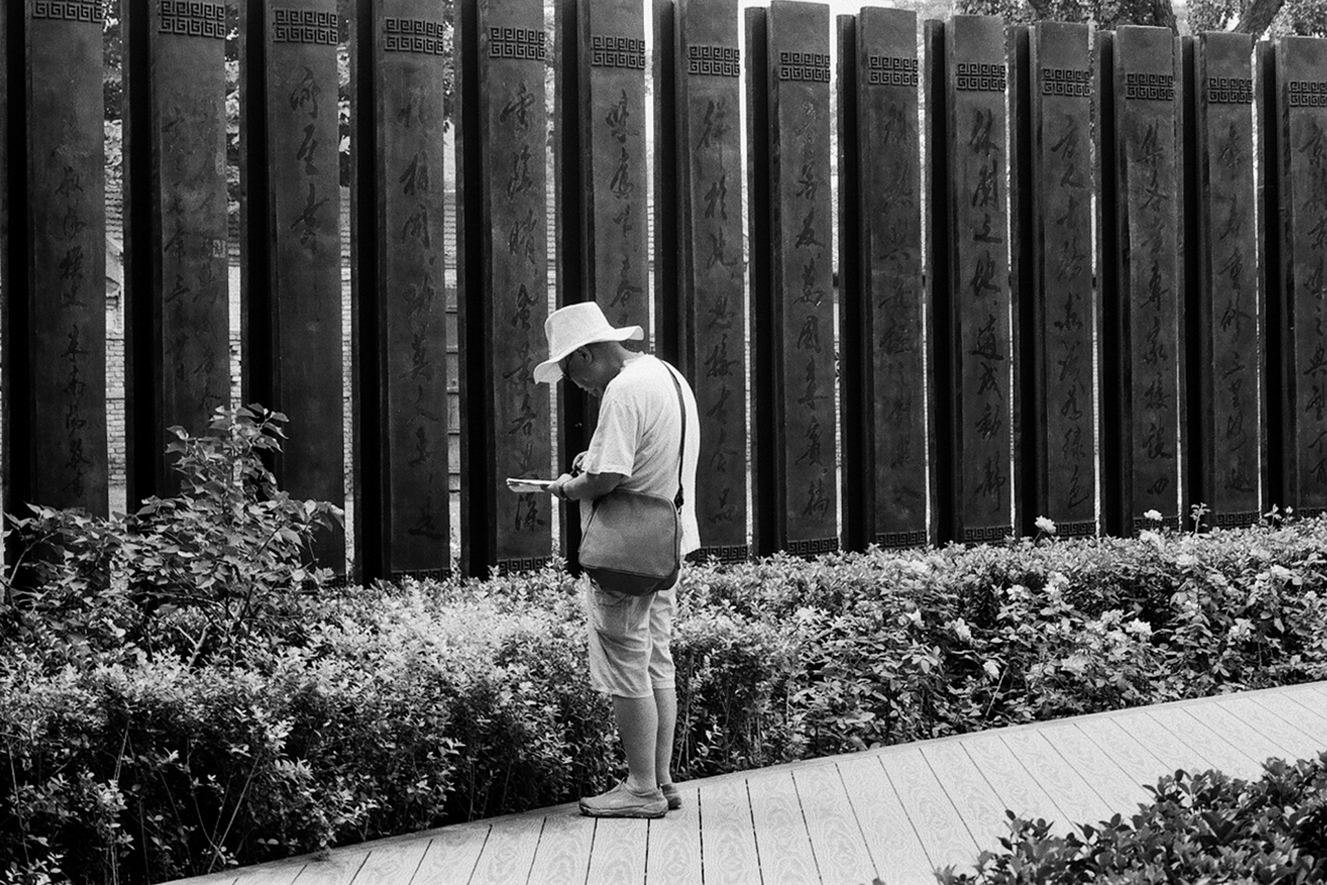Man in white clothes standing at wall of dark carved stone panels with Chinese characters