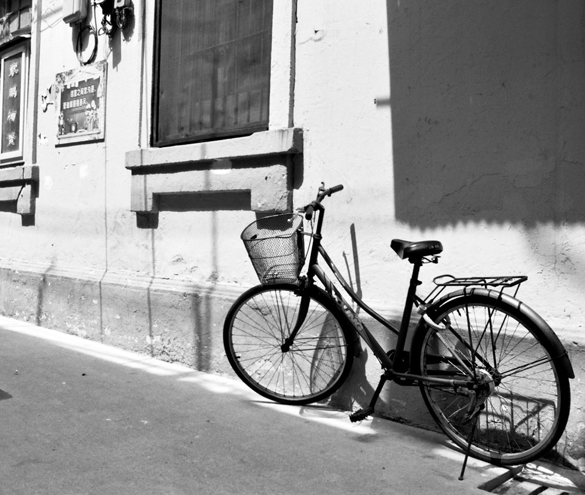 Bicycle with basket parked against white storefront with dramatic shadow cast on wall