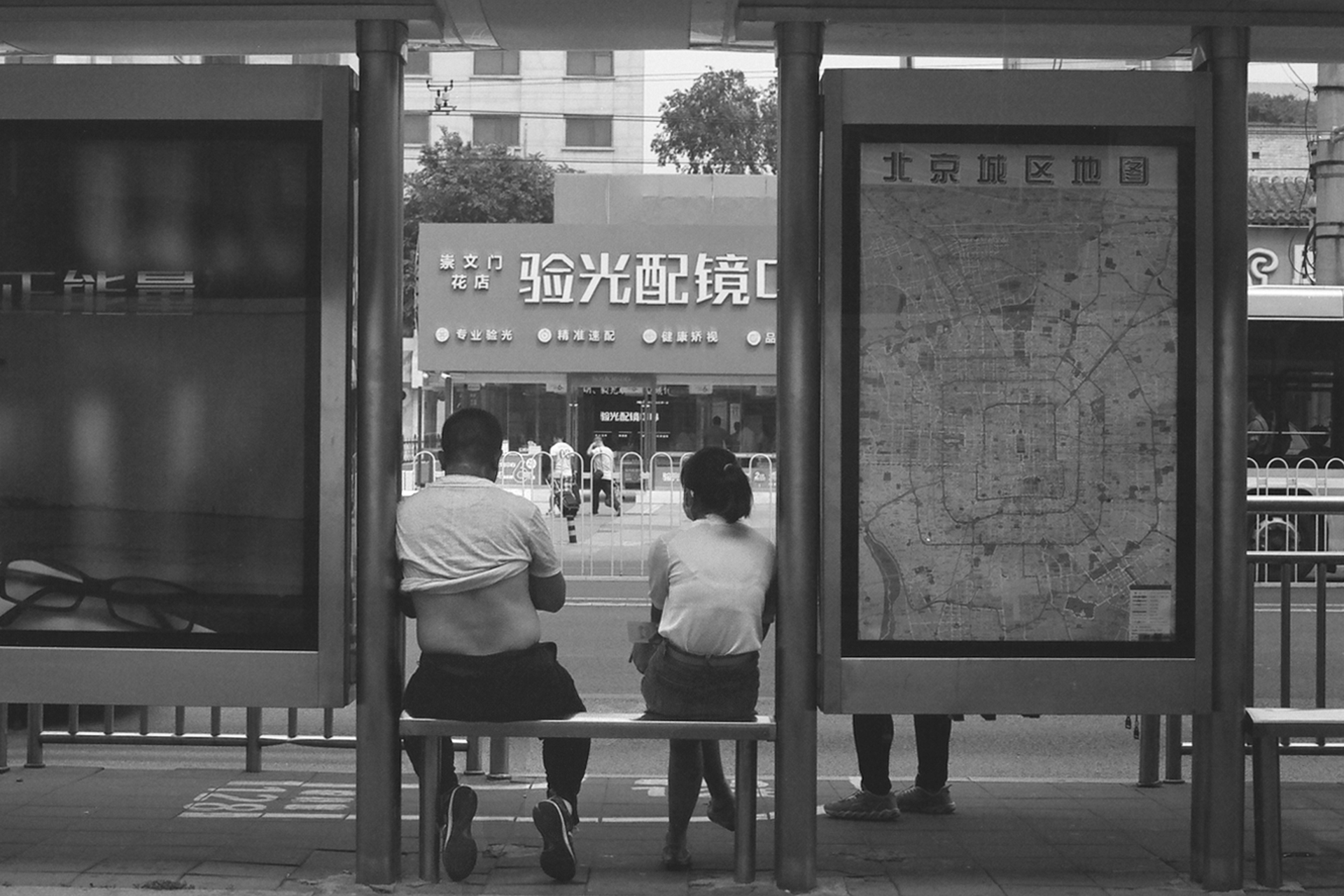 Bus stop shelter with two people viewing map and architectural glass panels reflecting surroundings