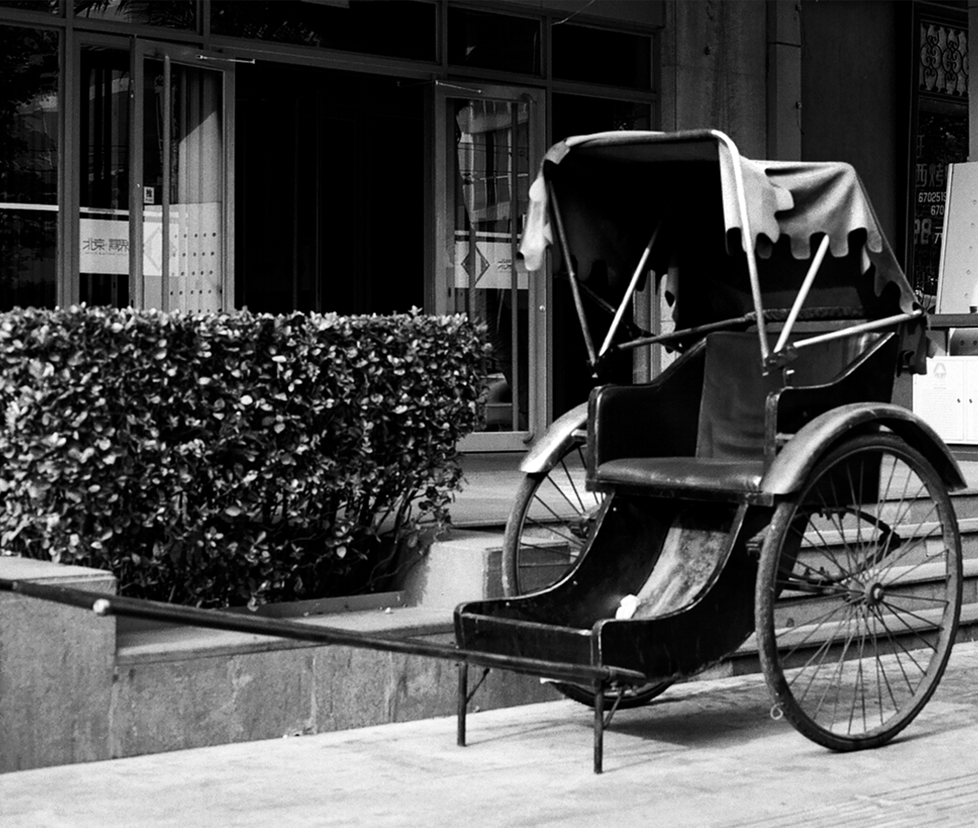 Traditional rickshaw with canvas tarp parked in front of storefront with vegetation and signage