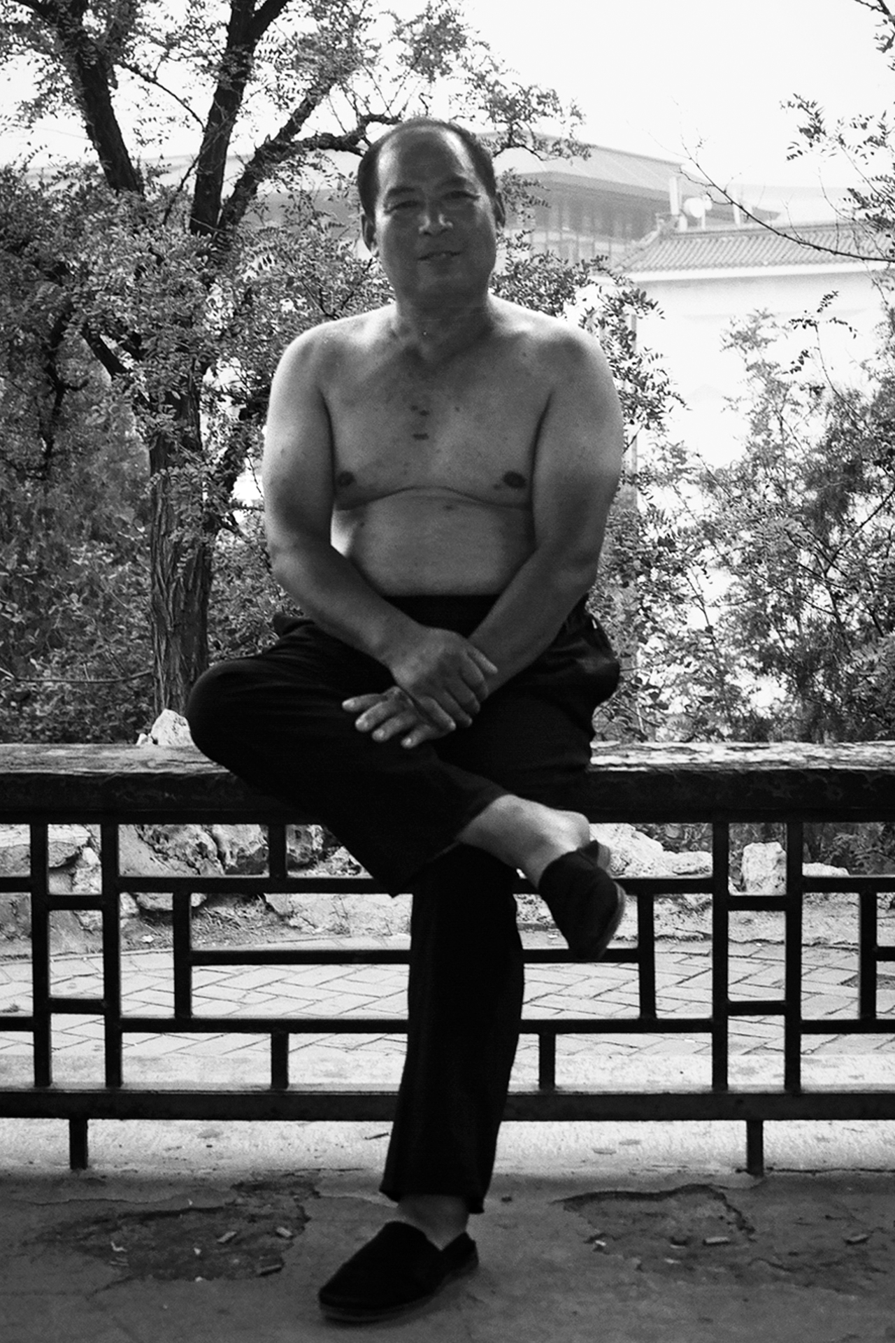 Man sitting on bench against trees with traditional building and water visible in background