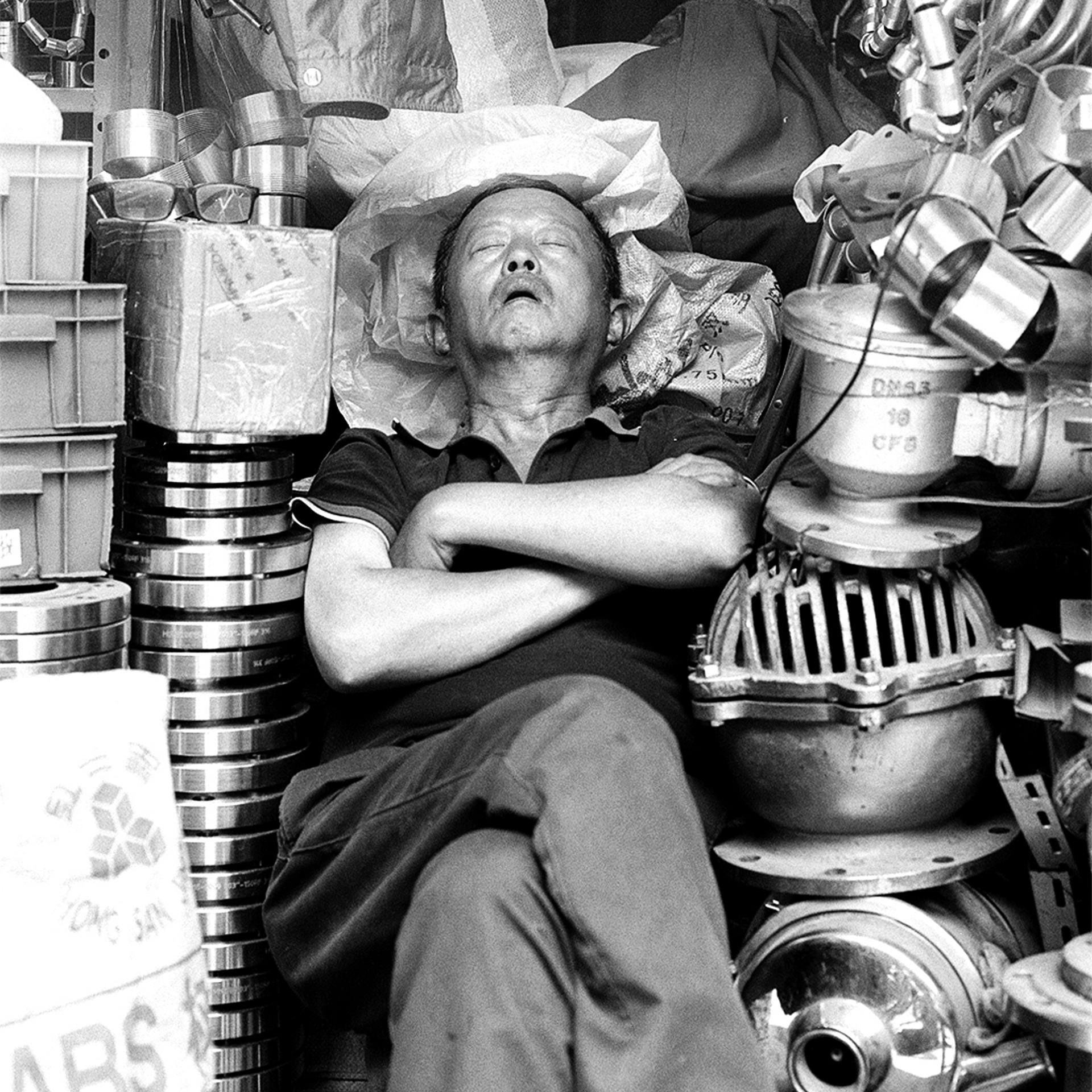 Man resting reclined among stacked metal cooking pots and household equipment containers