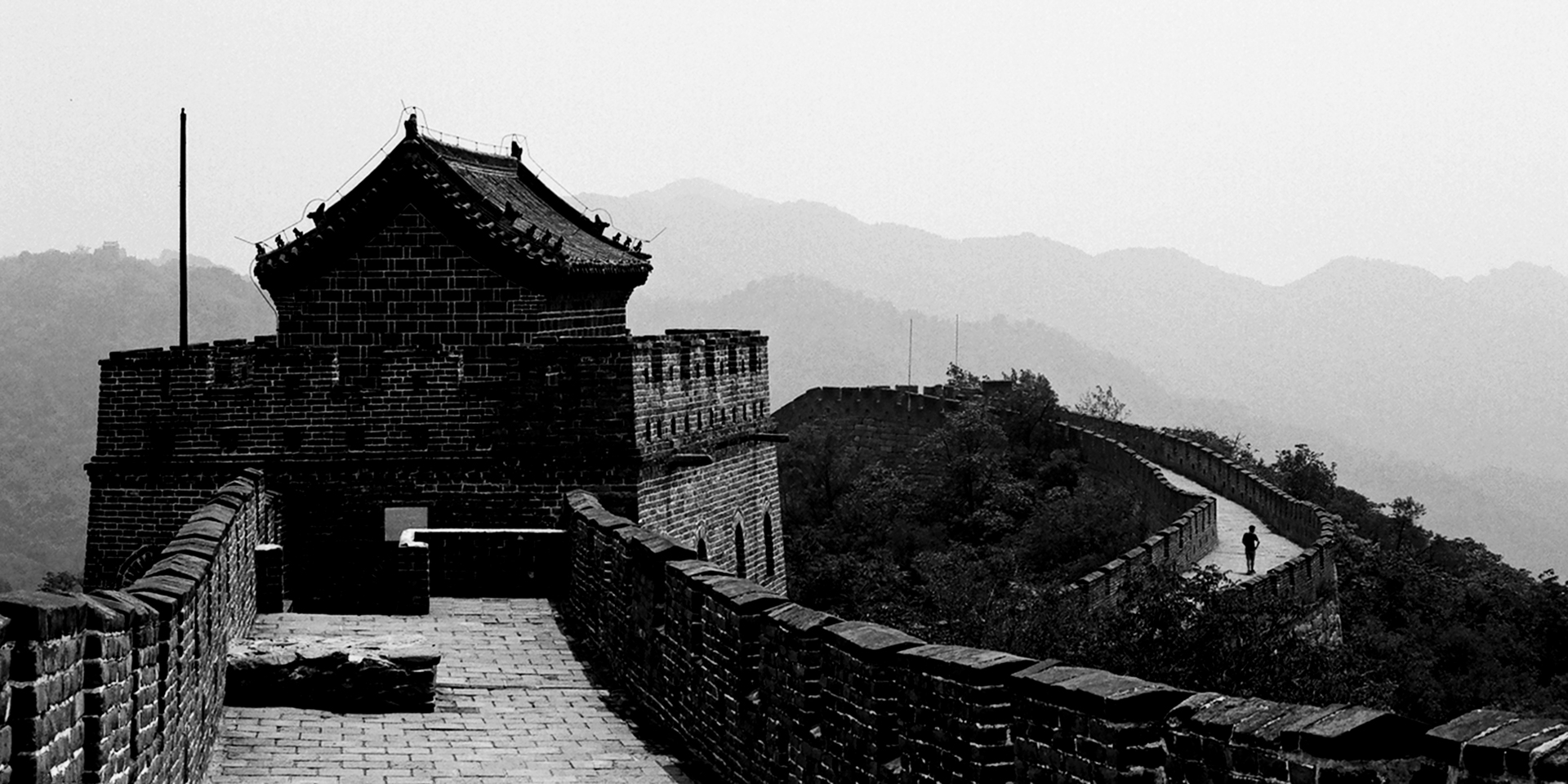 Great Wall section with watchtower and fortification rising through misty forested mountains
