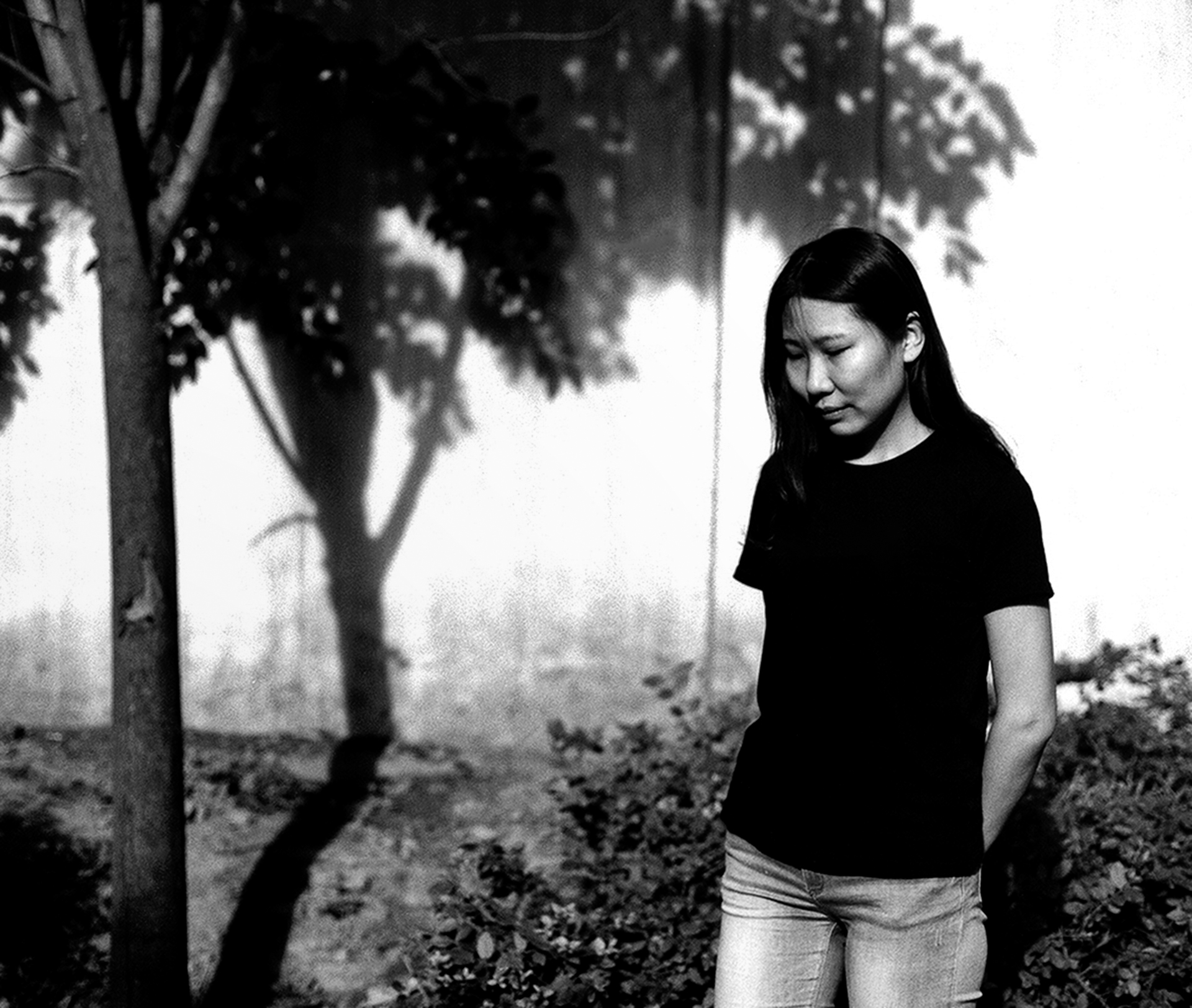 Woman standing under tree with dappled shadow against blurred foliage background in soft focus