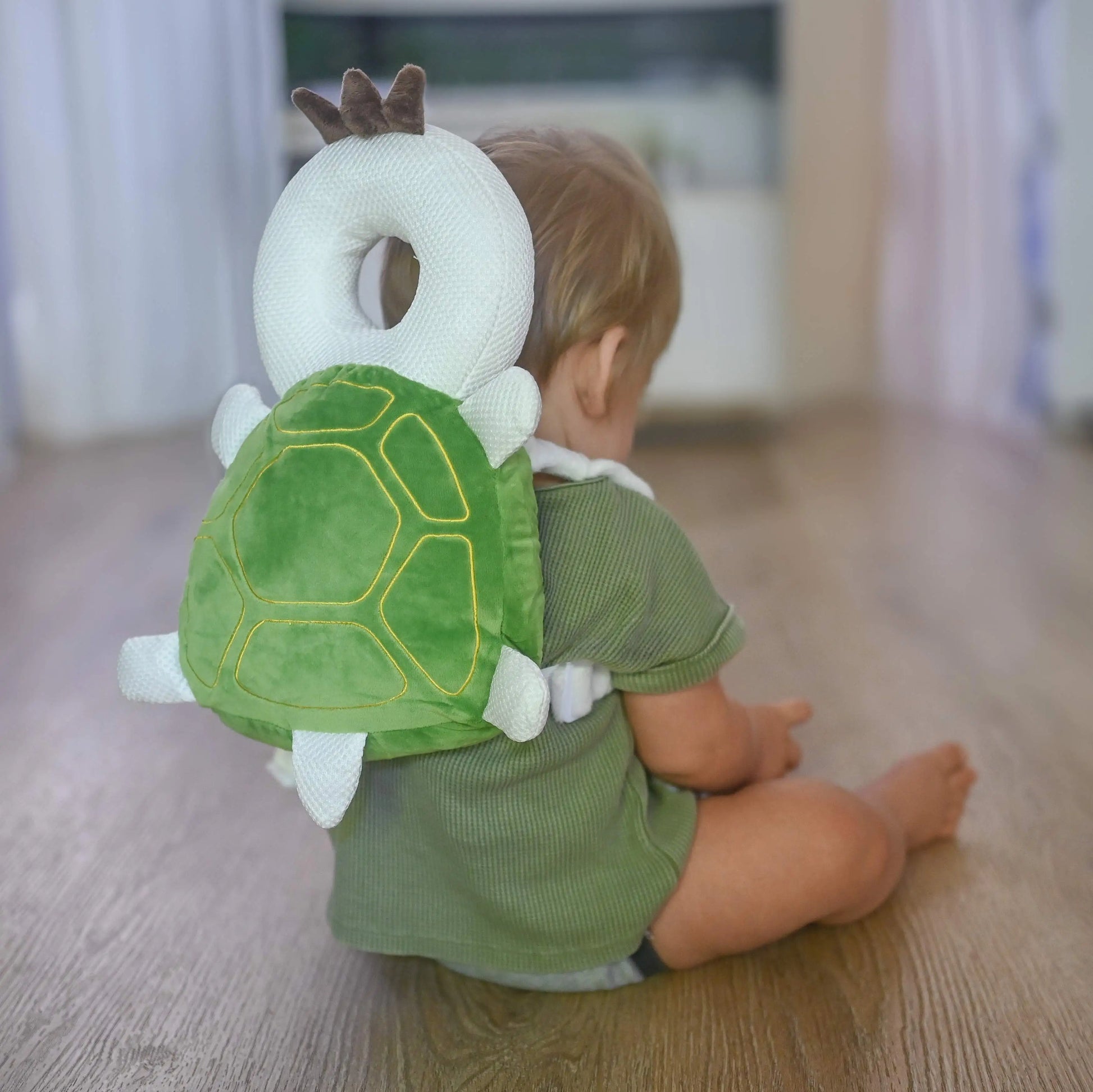 Baby wearing SafeYourBaby Turtle backpack, sitting on floor