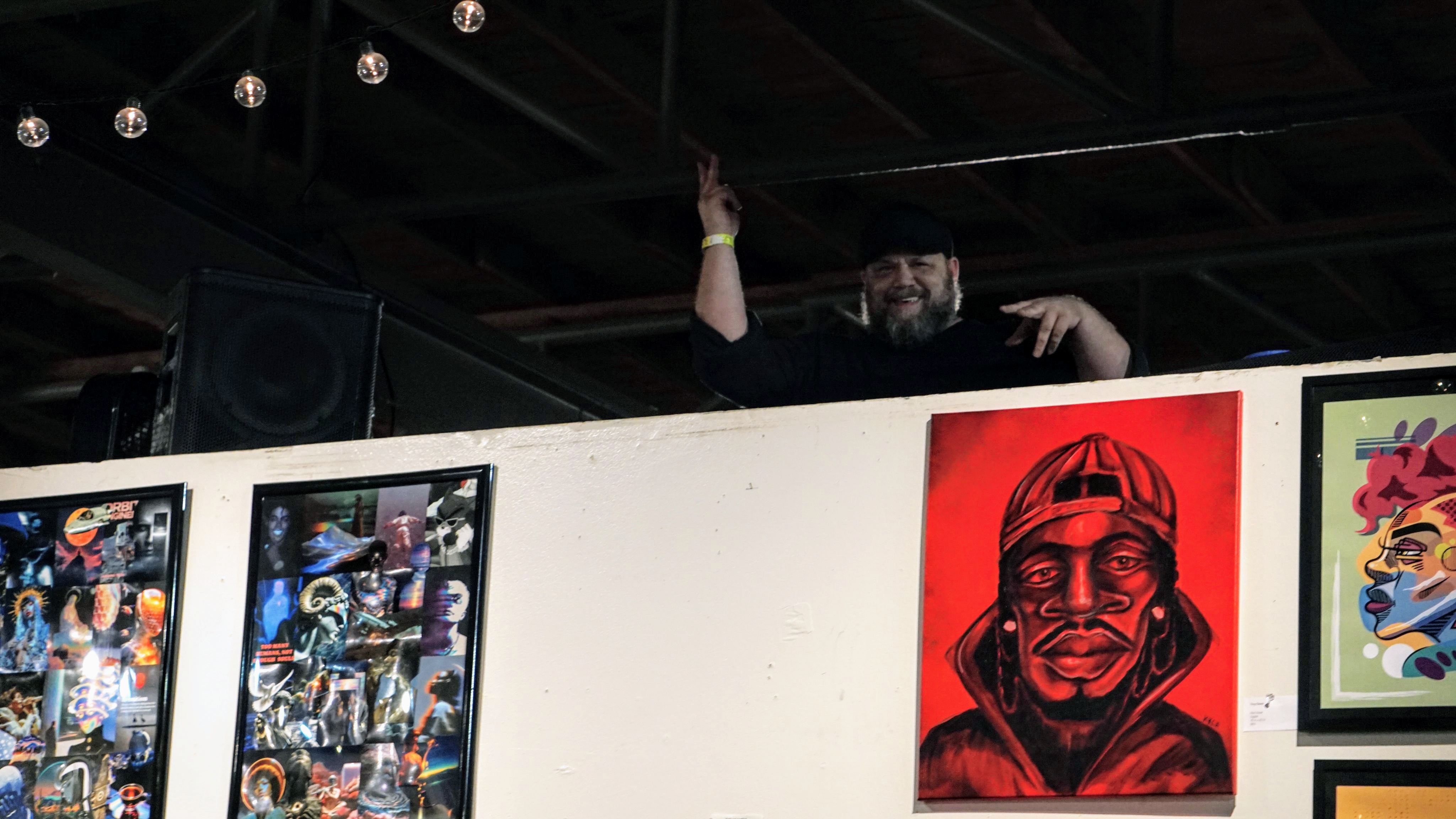 DJ performing above artwork display with red portrait
