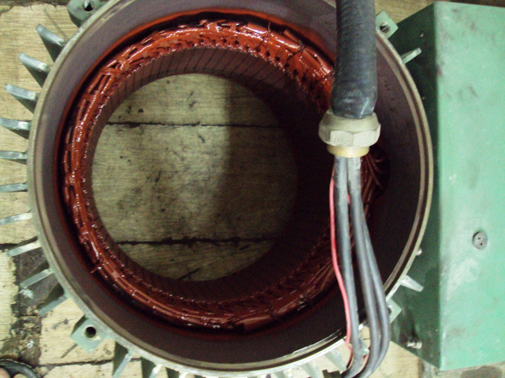 Veliki transformator ili motor stator sa crvenim/smeđim bakrenon zavojima i metalnim jezgrom