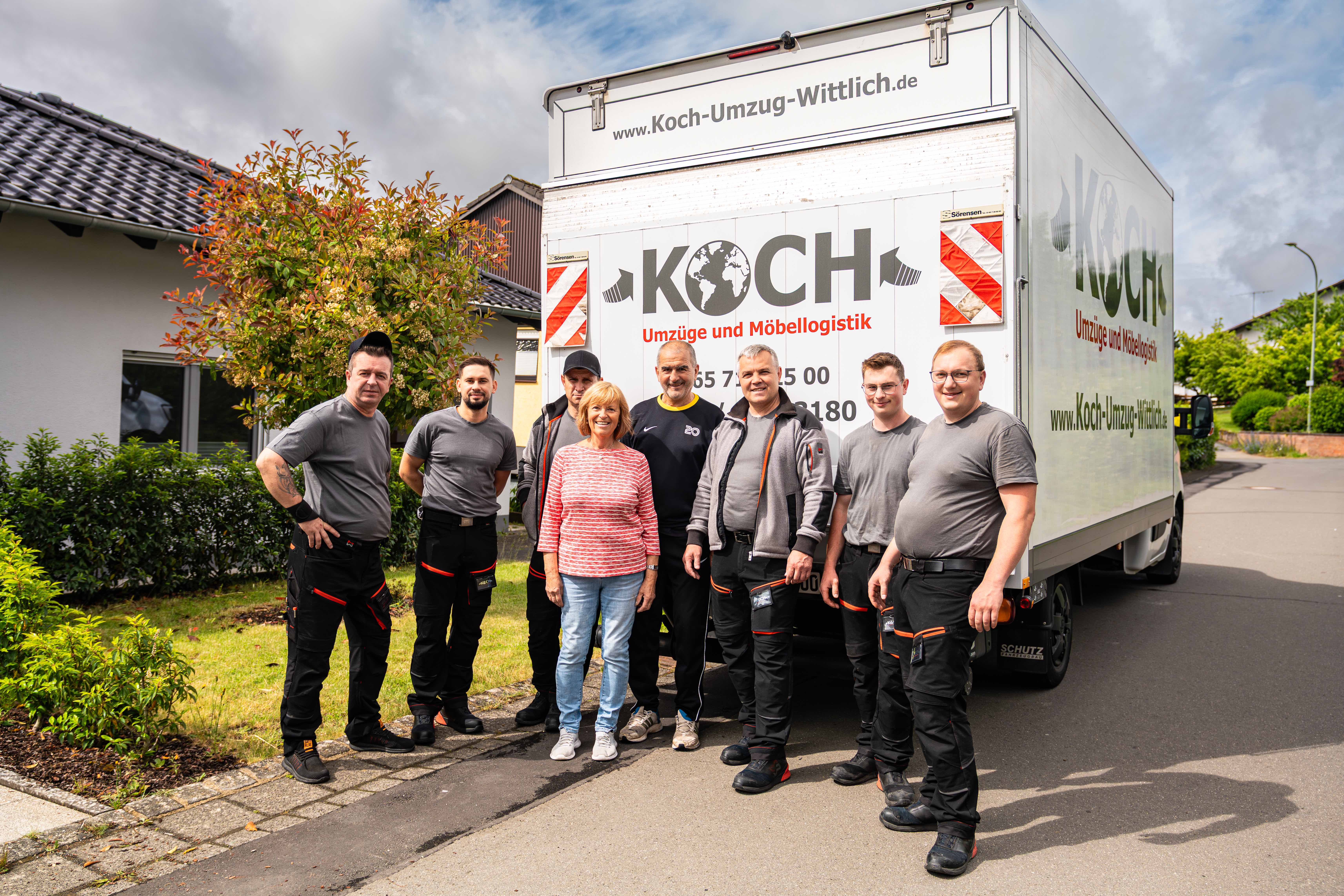 Koch Umzüge Team mit zufriedener Kundin vor dem Firmenfahrzeug